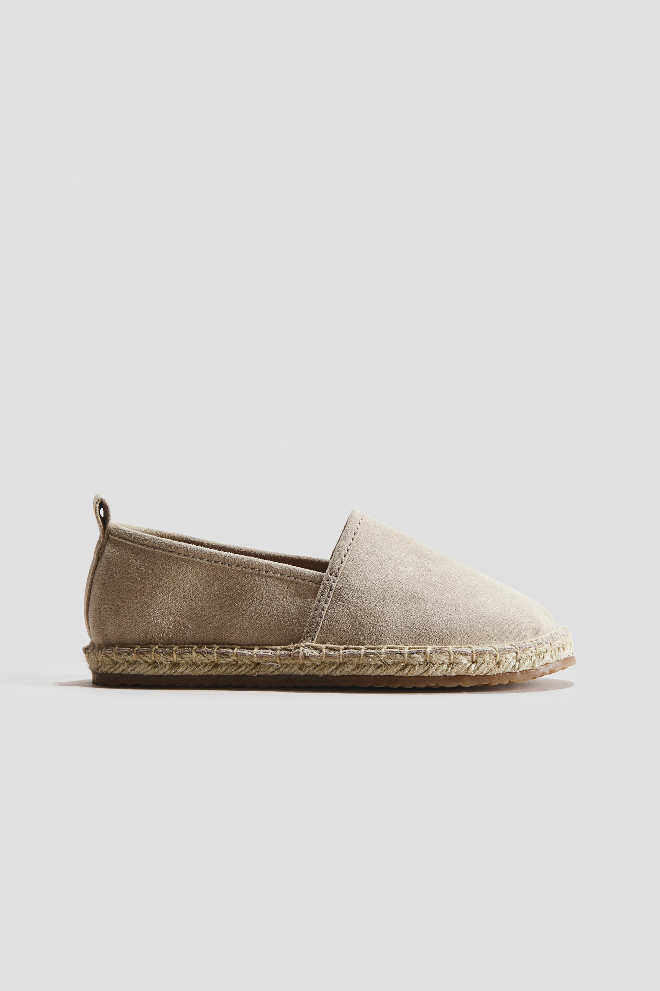 Grotere afbeelding bekijken: Een lichtbruine suède espadrille toont zijn zijprofiel, met een gestikte jutezool, een dunne bruine rubberen buitenzool en een klein treklusje aan de hiel.