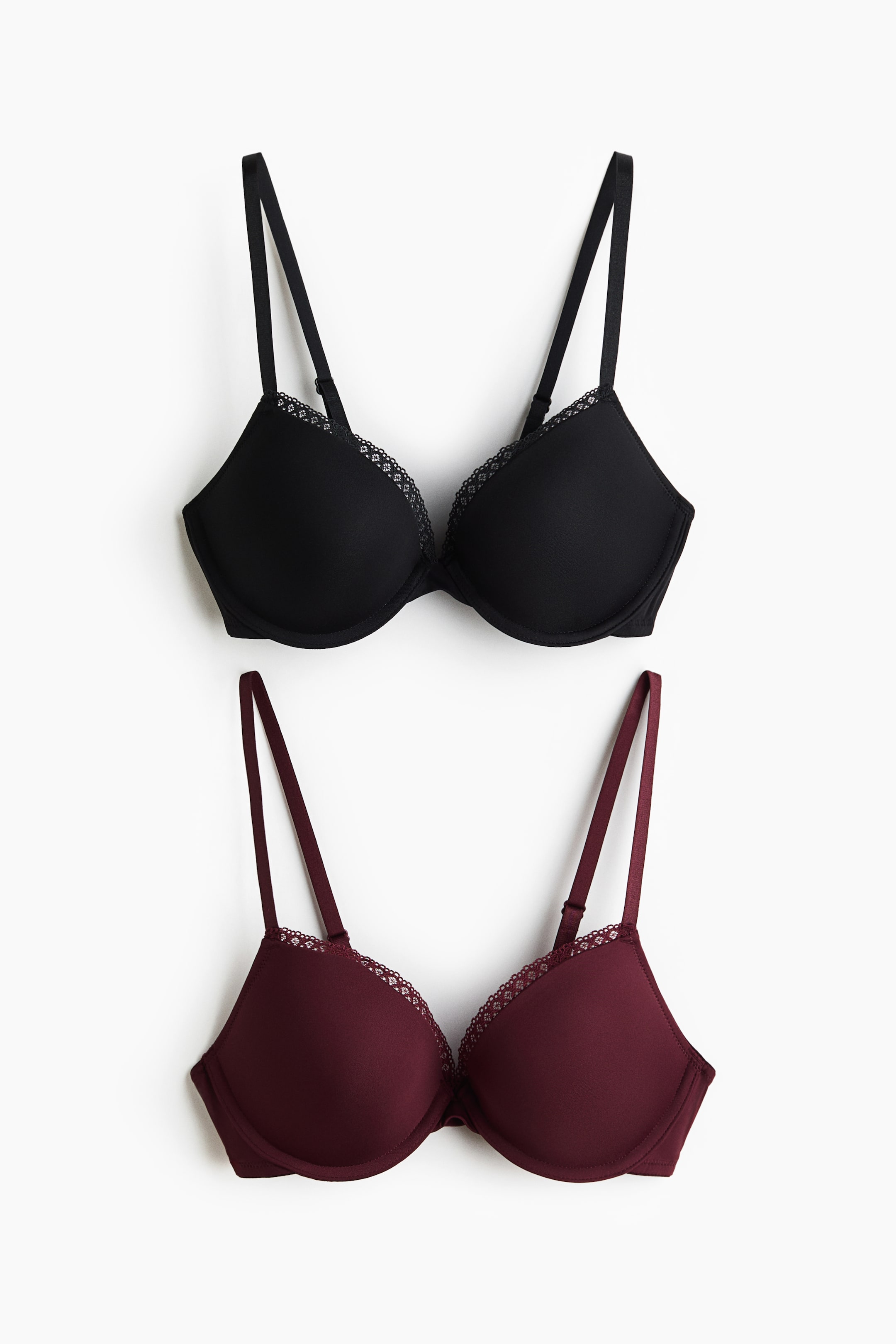 Agrandir l'image: Deux soutiens-gorge push-up sont posés à plat, l’un noir et l’autre bordeaux. Tous deux présentent des bonnets lisses avec une délicate finition en dentelle le long des bords supérieurs et des bretelles réglables.