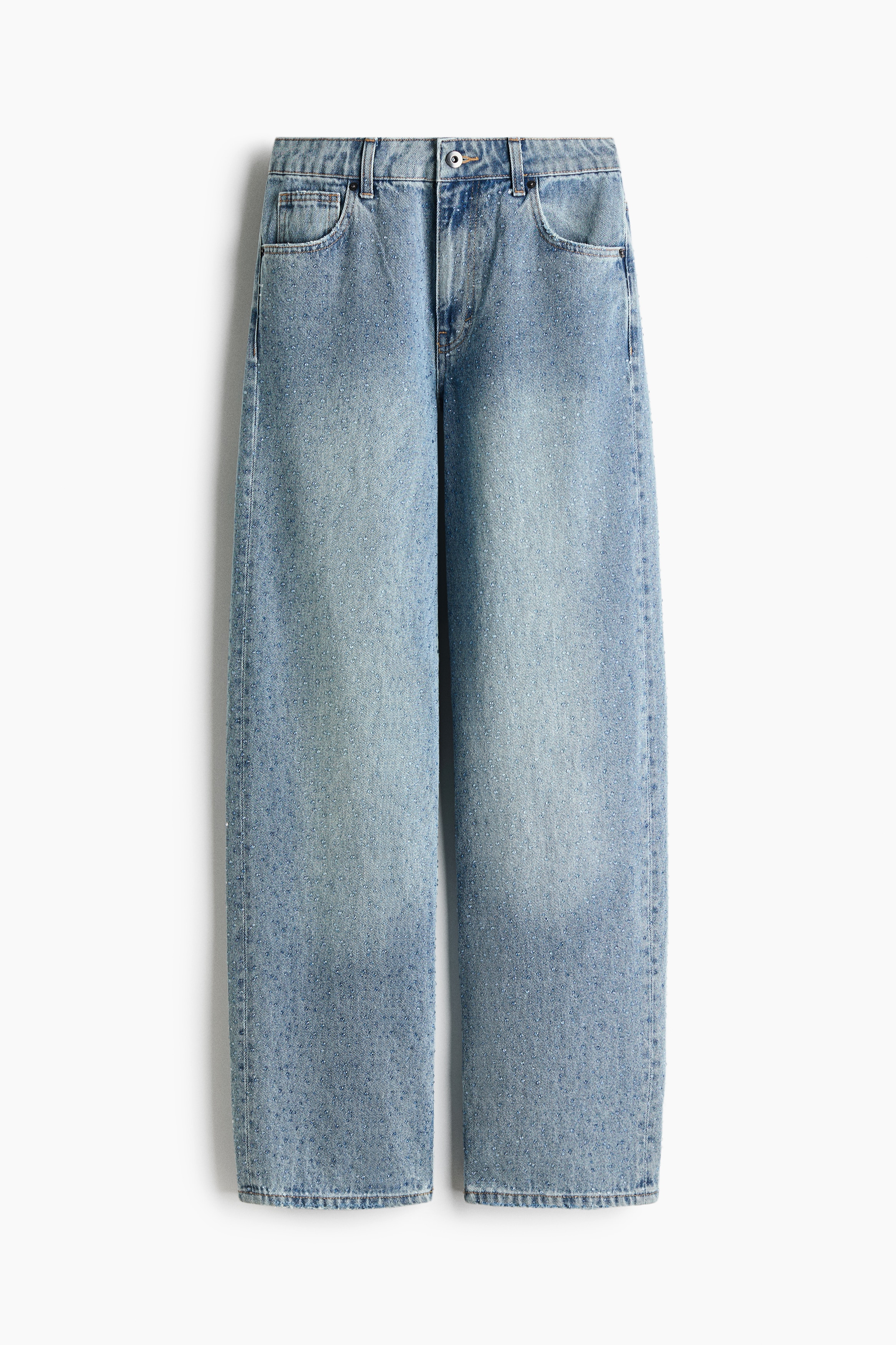 Jeans in denim azzurro chiaro a gamba ampia, impreziositi da decorazioni scintillanti all-over, indossati dalla modella. I jeans dalla vestibilità rilassata a cinque tasche sono abbinati a una blusa bianca a maniche lunghe con volant.
