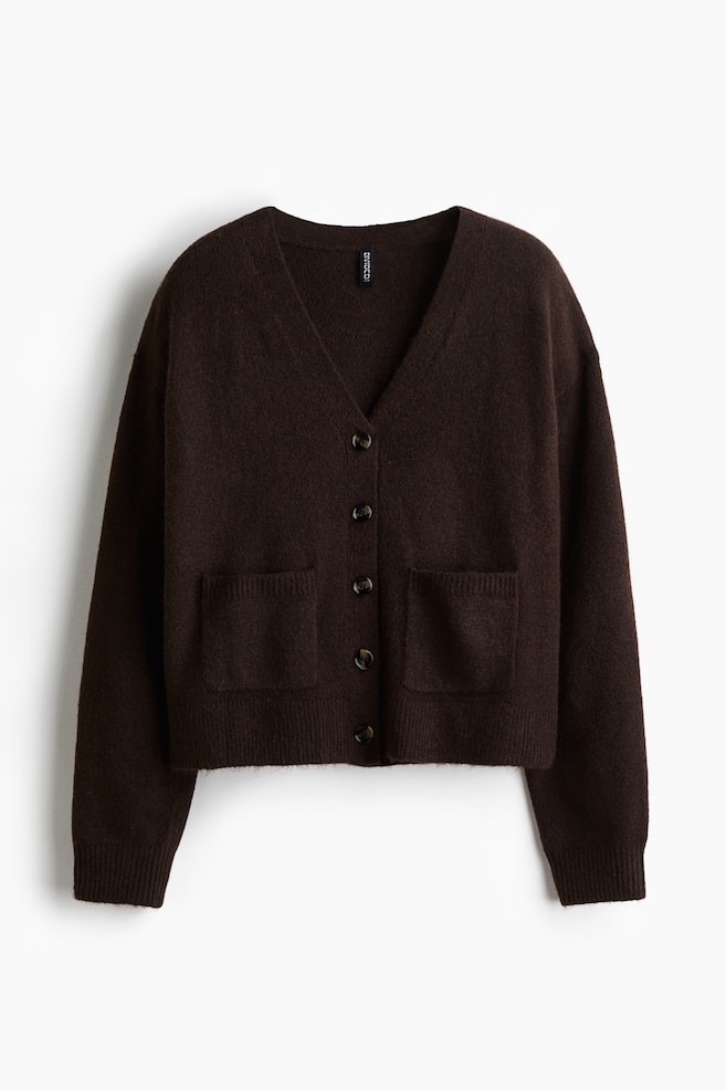 A front-facing, dark brown, loose-fit cardigan in a soft knit is displaying a V-shaped neckline with five buttons down the front. It is featuring dropped shoulders, long sleeves, and two open front pockets, with visible ribbing at the cuffs and hem. - 1
