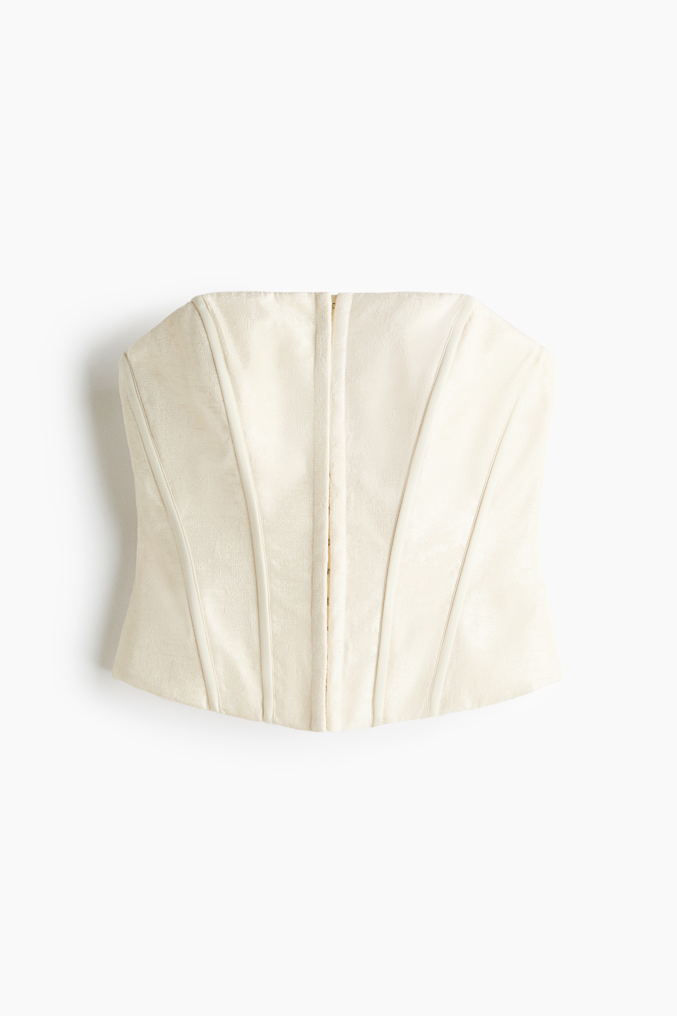 Un haut corset jacquard de couleur crÃ¨me, dotÃ© dâarmatures verticales et dâune fermeture sur le devant, est portÃ© par le mannequin, superposÃ© Ã  un pull en maille blanc Ã  col montant. Le mannequin se tient debout, une main posÃ©e sur la hanche, mettant en valeur la coupe structurÃ©e du corset.