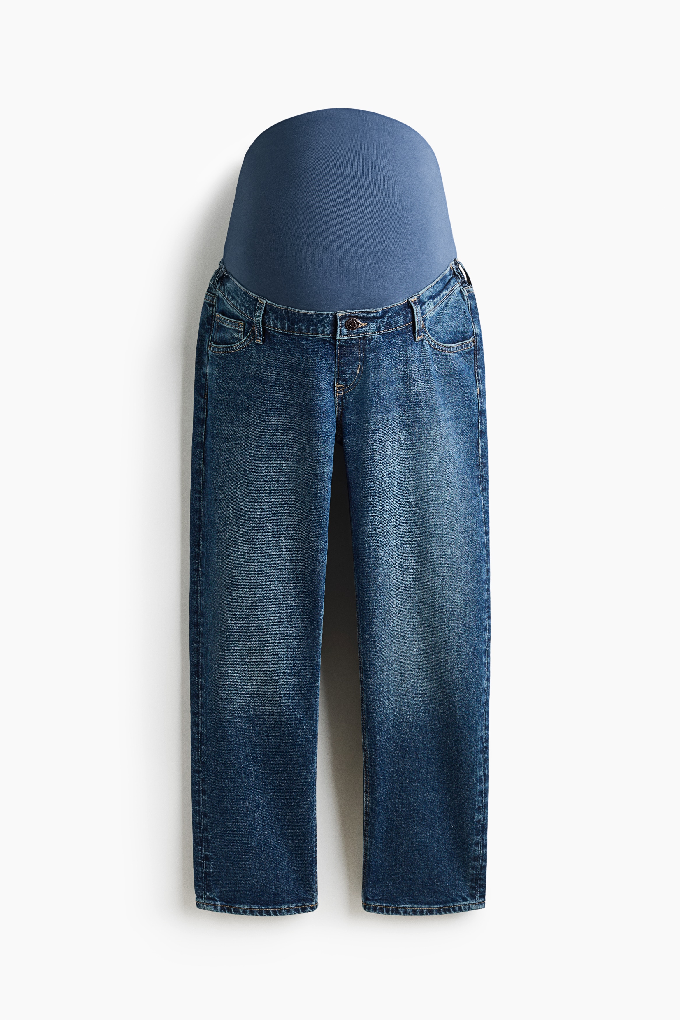 Modelen bÃ¦rer mellemvaskede blÃ¥ denimmammabukser med falsk gylp og knap, stylet med en mÃ¸rk langÃ¦rmet top og blÃ¥ sneakers. En grÃ¥ og marineblÃ¥ argyle-sweater er draperet over modelens skuldre og komplementerer de ankellange jeans med smalle ben.