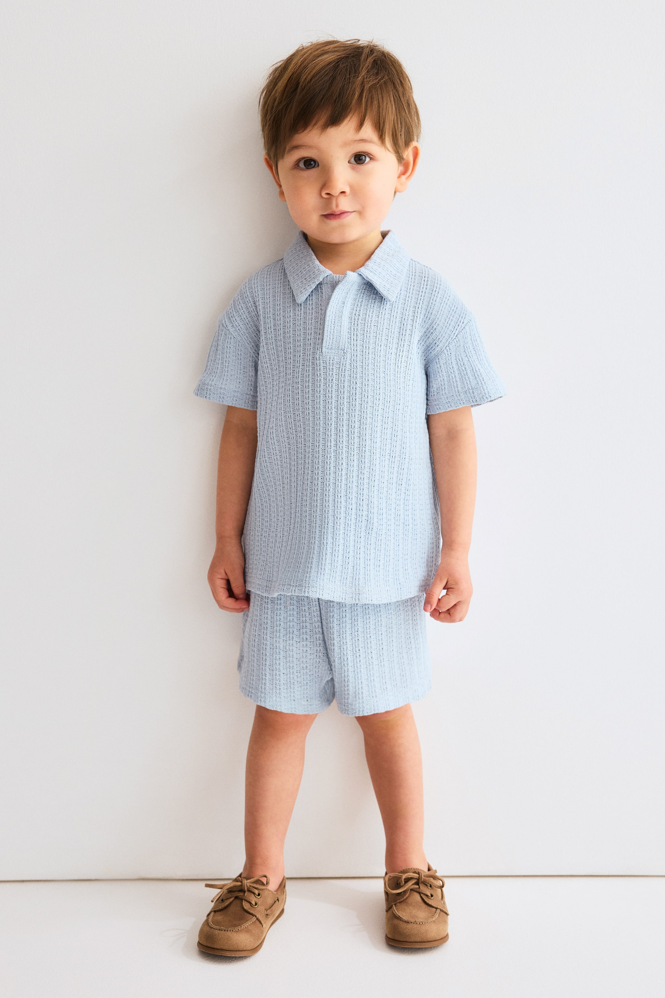 Voir une image plus grande: Un ensemble deux pièces bleu clair présente un haut de style polo et un short assorti, tous deux en tissu tricoté texturé. Le haut est doté d'un col classique, d'une courte patte de boutonnage et de manches courtes amples, tandis que le short offre une coupe décontractée, se terminant à mi-cuisse.