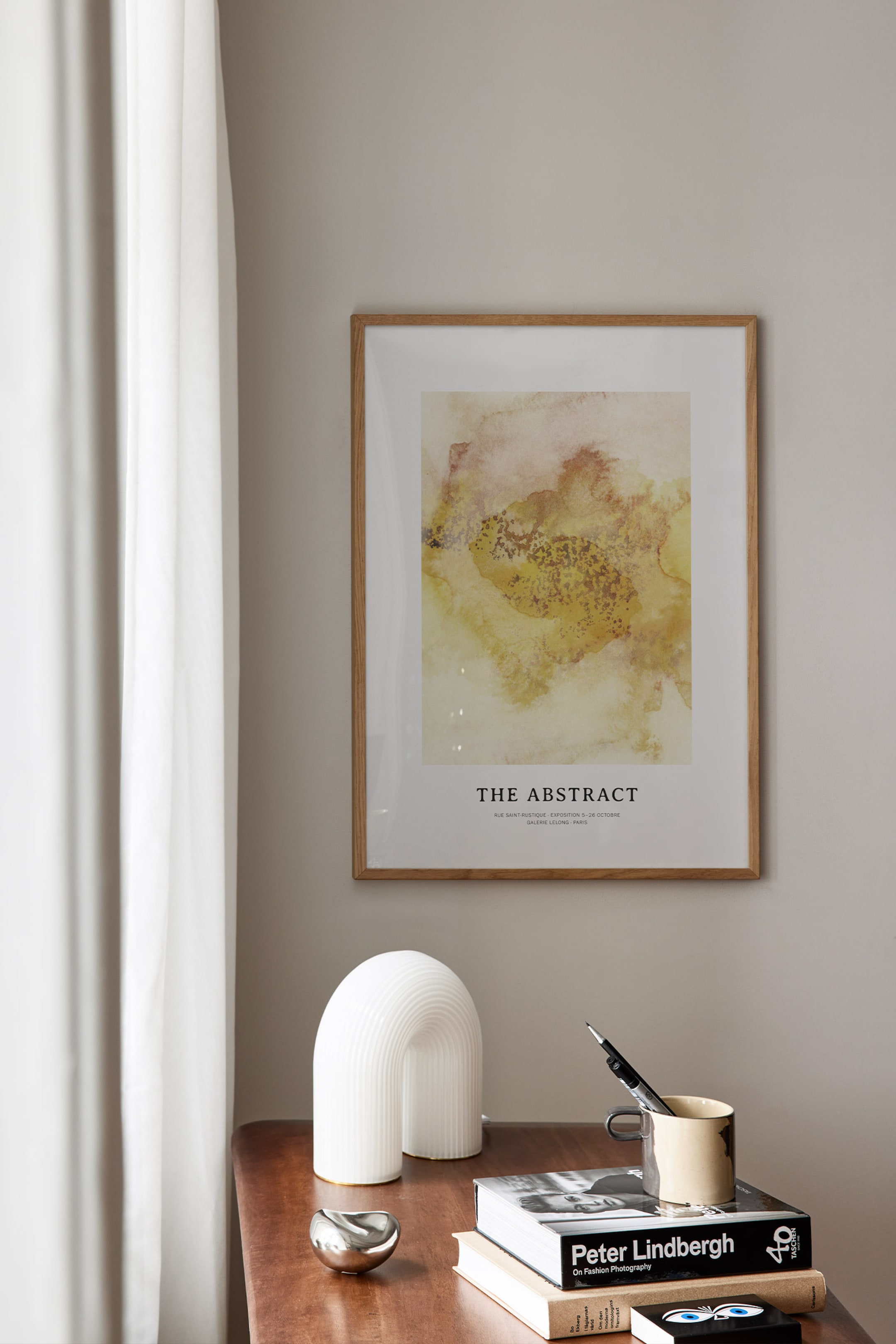 Grotere afbeelding bekijken: Een ingelijste kunstdruk hangt recht vooruit en toont een abstracte compositie van warme gele, oranje en bruine tinten met gespikkelde texturen. De print draagt de titel "THE ABSTRACT" en heeft extra tekst eronder, alles omsloten door een lichte houten lijst.