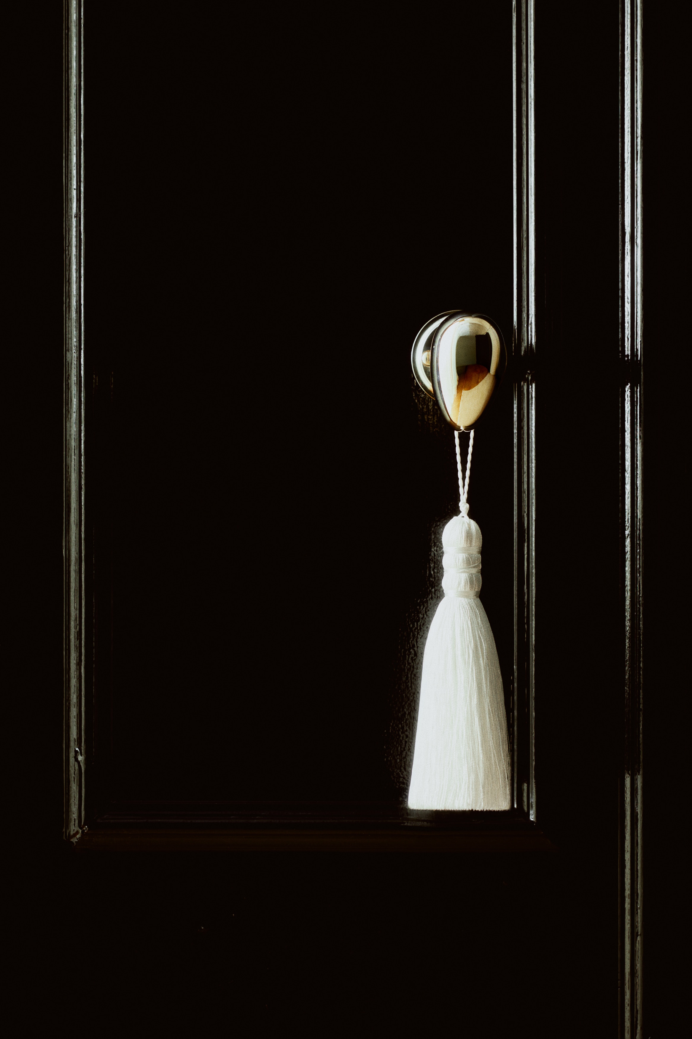 Two white tassel ornaments are hanging side-by-side, facing forward, with each ornament featuring a long twisted cord hanging loop, a wrapped decorative neck, and a straight, fine-threaded tassel skirt.