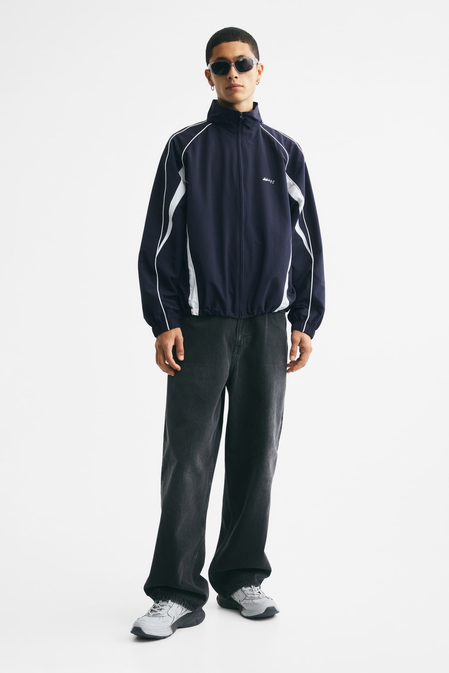 A navy blue track jacket is showcased with a full-zip front, a stand-up collar, and a small white logo on the left chest. It features white piping along the raglan seams and white side panels, complete with elasticated cuffs and hem. - 1