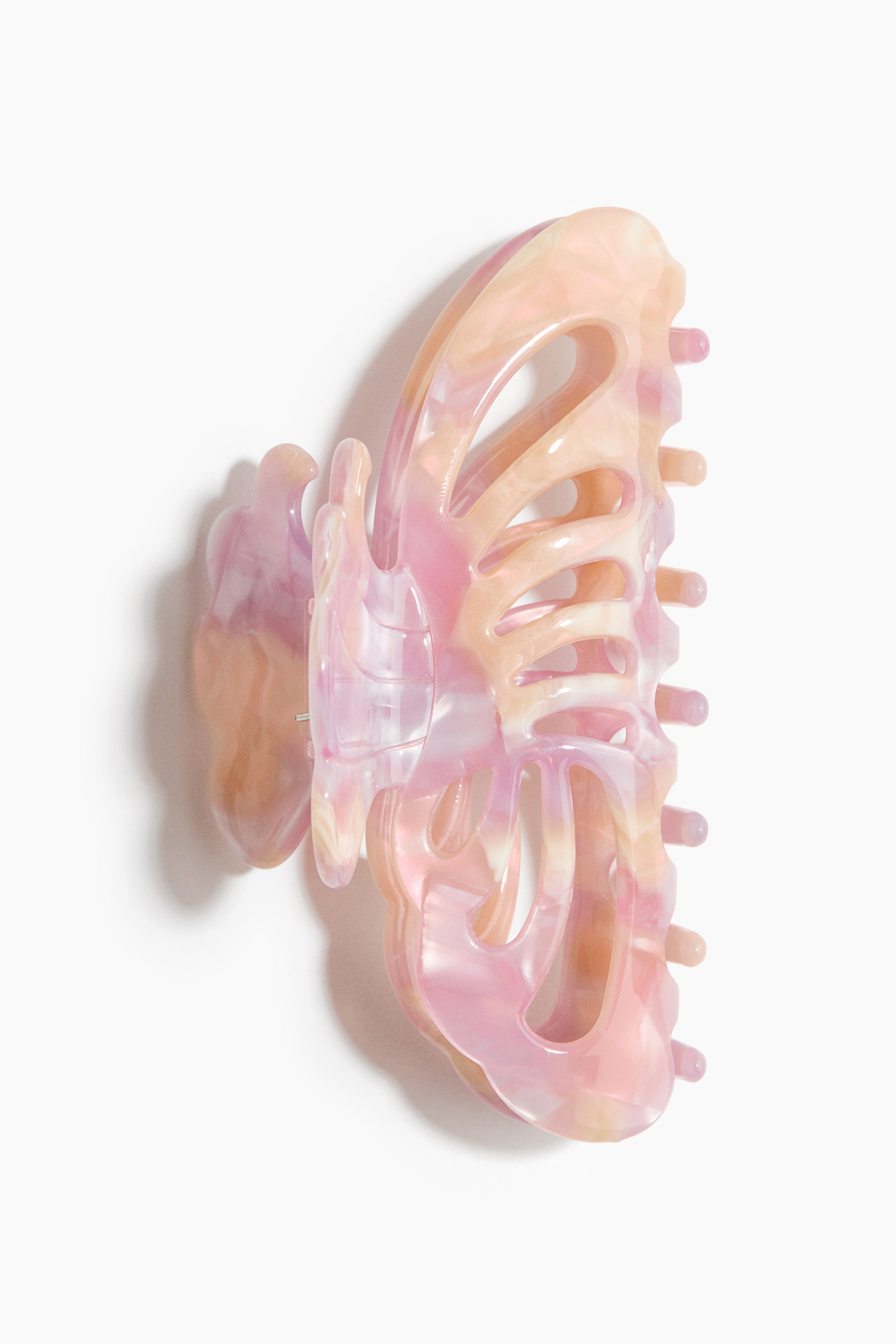 Ver imagem maior: Um gancho de cabelo em plástico com acabamento brilhante apresenta um design inspirado numa borboleta, com um padrão marmoreado em rosa pastel, pêssego e creme. A mola mostra dentes curvos interligados ao longo de um dos lados e uma dobradiça com mola no centro, destacando a sua estrutura num perfil lateral.