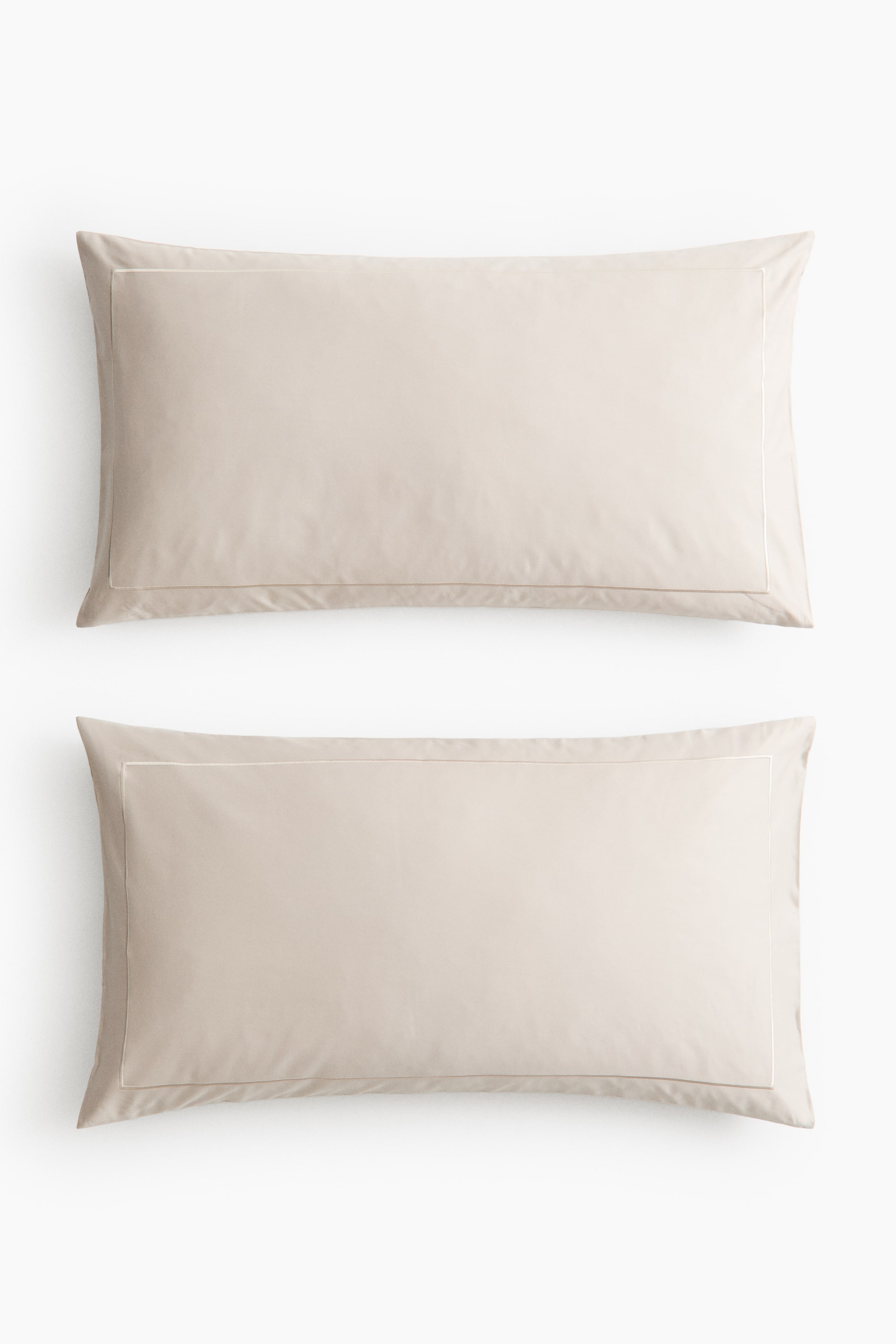 View larger image: Two rectangular pillowcases showcase a light beige hue. Each pillowcase features a single stitched line forming a rectangular border on its front side.
