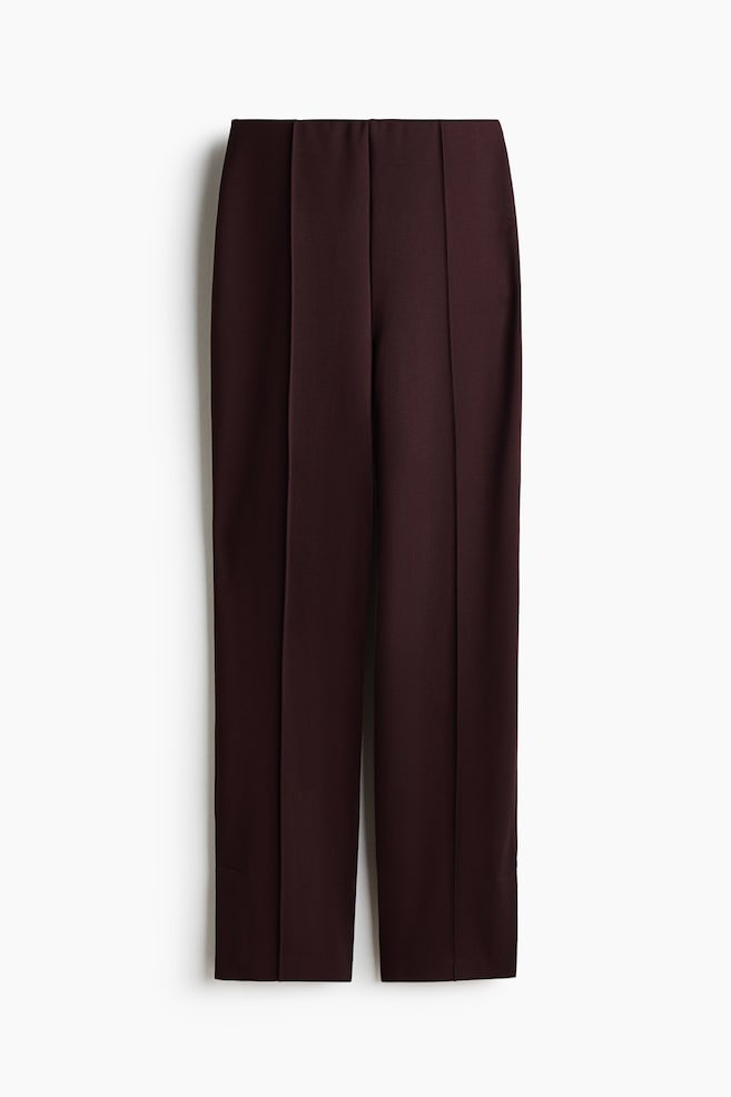 Dark red pants are displaying a flat-front waistband with vertical stitched creases running down the front of each straight, slightly cropped leg. - 1