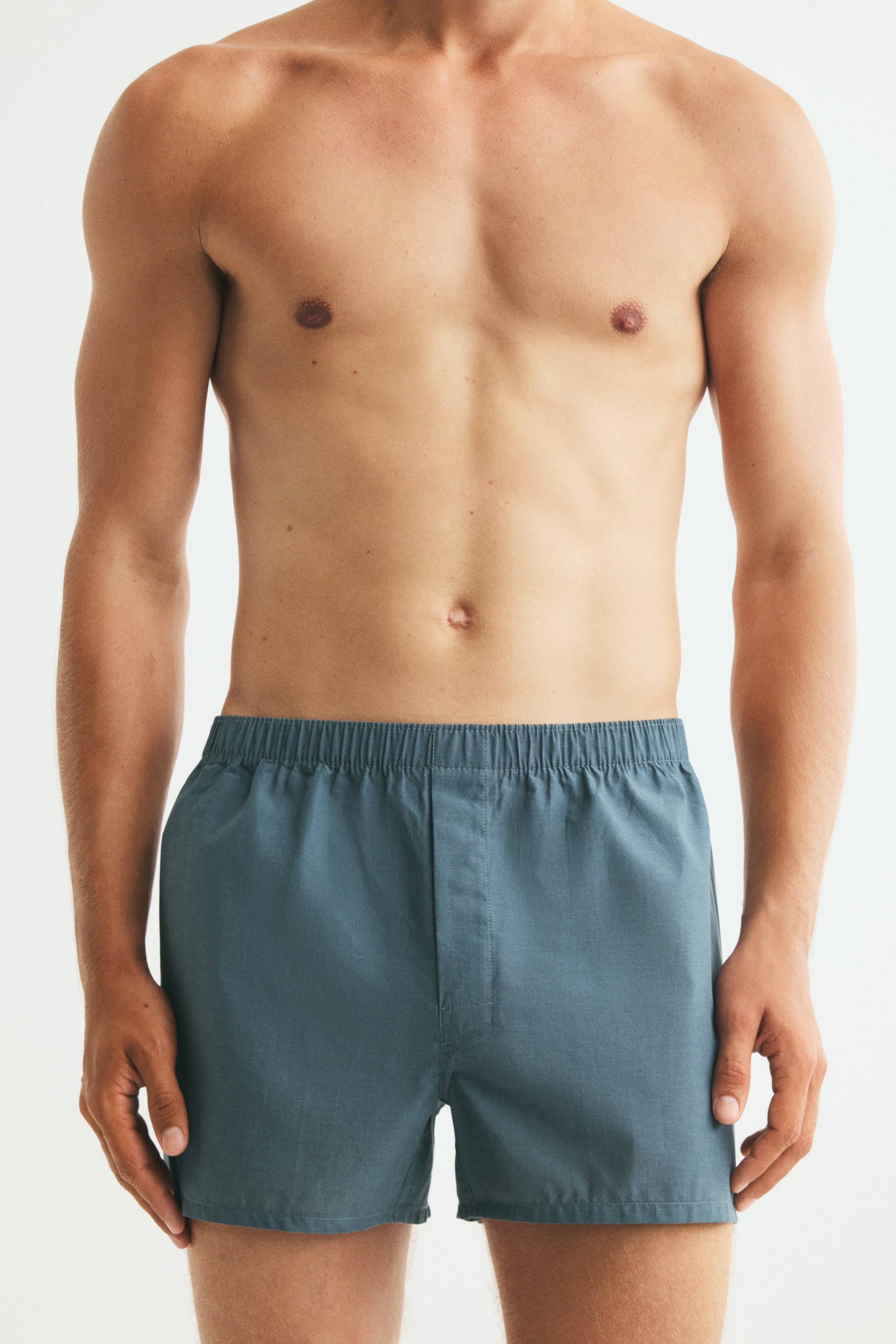 Vier Paar Boxershorts liegen flach da und zeigen ihre oberen Vorderteile und elastischen Taillenbänder. Ein Paar ist uni türkis, zwei Paare haben ein türkis und grün kariertes Design, und das vierte Paar ist hellblau mit weißen vertikalen Streifen.