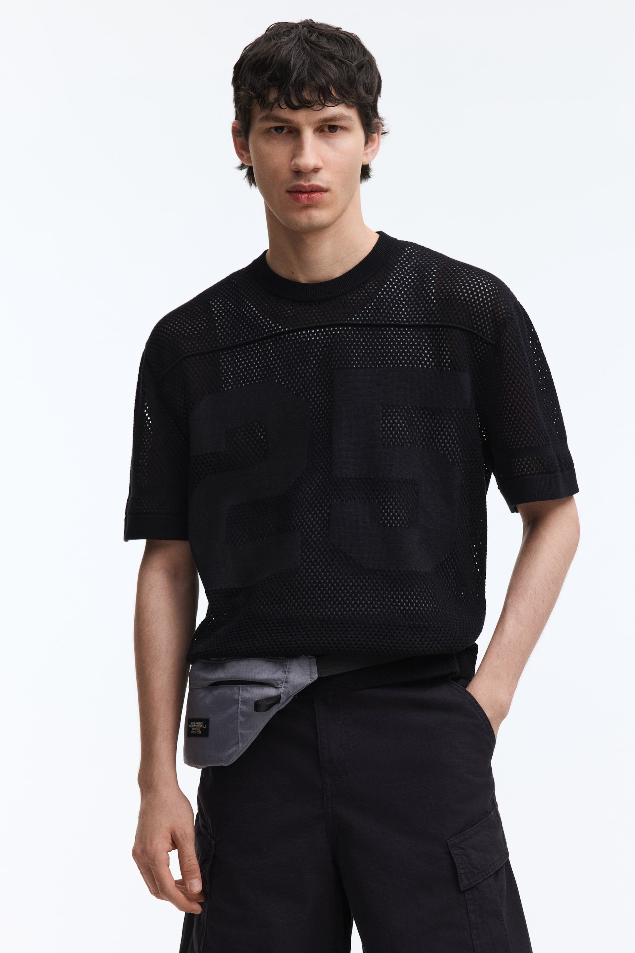 Ampliar la imagen: Una camiseta de malla negra presenta un diseño grande de "25" en tejido sólido en la parte frontal, junto con rayas horizontales de tejido sólido a través del pecho superior. Está diseñada con mangas cortas con dobladillos de tejido sólido y un cuello redondo acanalado.