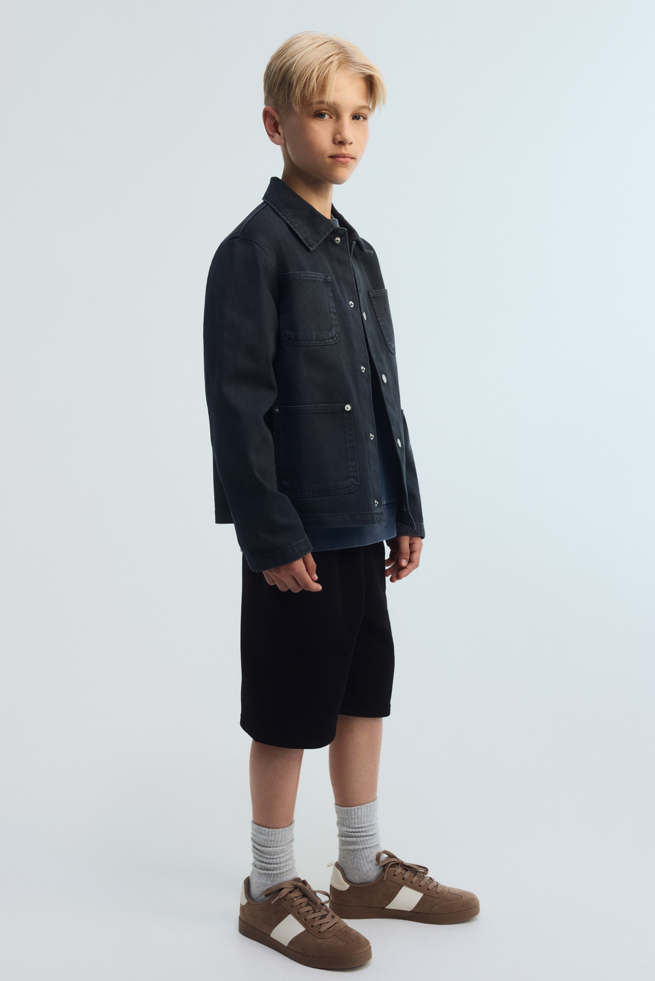 Agrandir l'image: Les shorts noirs longueur genou sont confectionnés dans un tissu de sweat, offrant une coupe décontractée vue d'un léger angle latéral. Les coutures latérales sont légèrement positionnées vers l'avant.