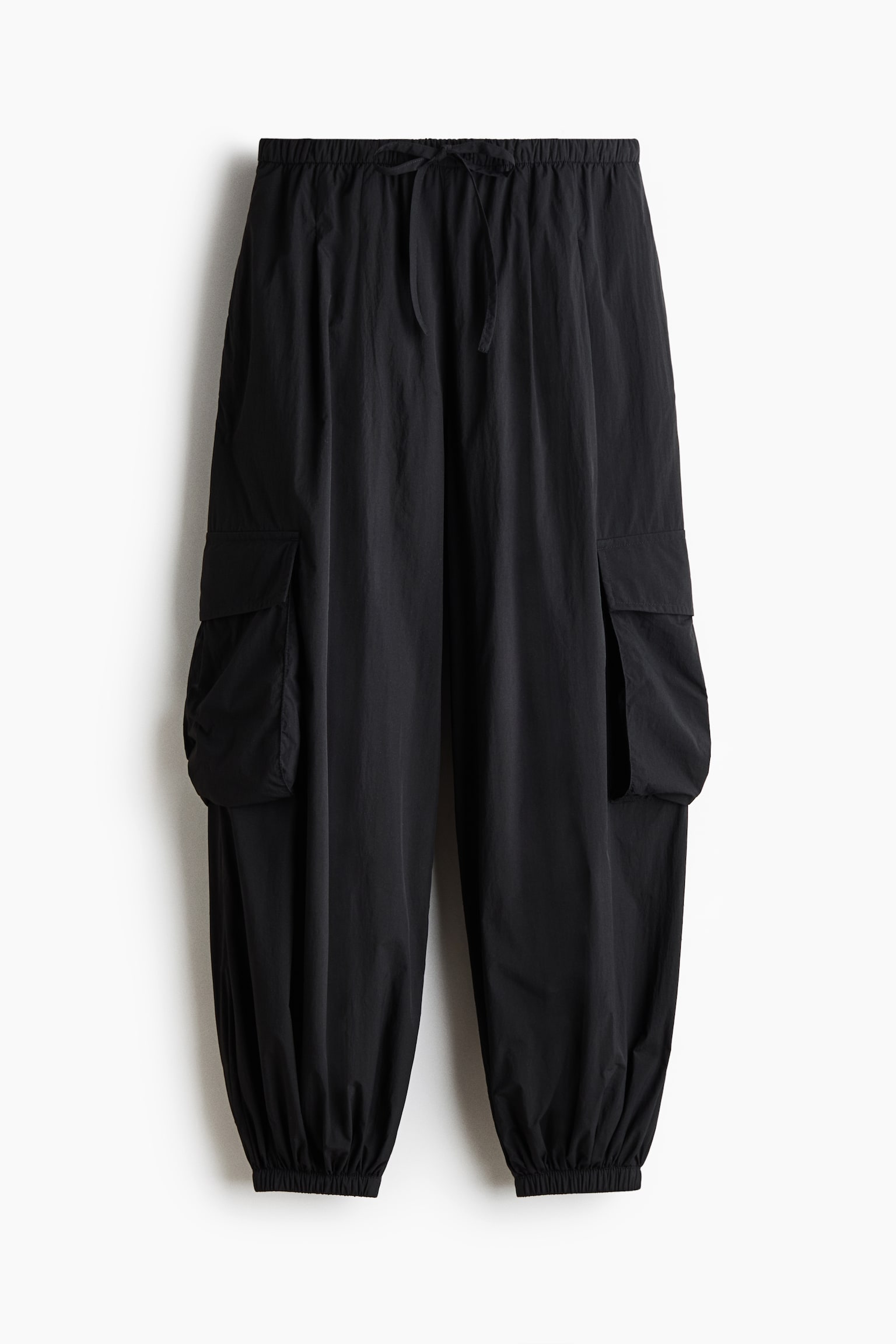 "Cargo pants hitam ini dipaparkan dari pandangan depan, menonjolkan pinggang elastik dengan tali serut, dua poket kargo besar dengan penutup pada setiap kaki, dan manset elastik berkumpul di pergelangan kaki." - 1