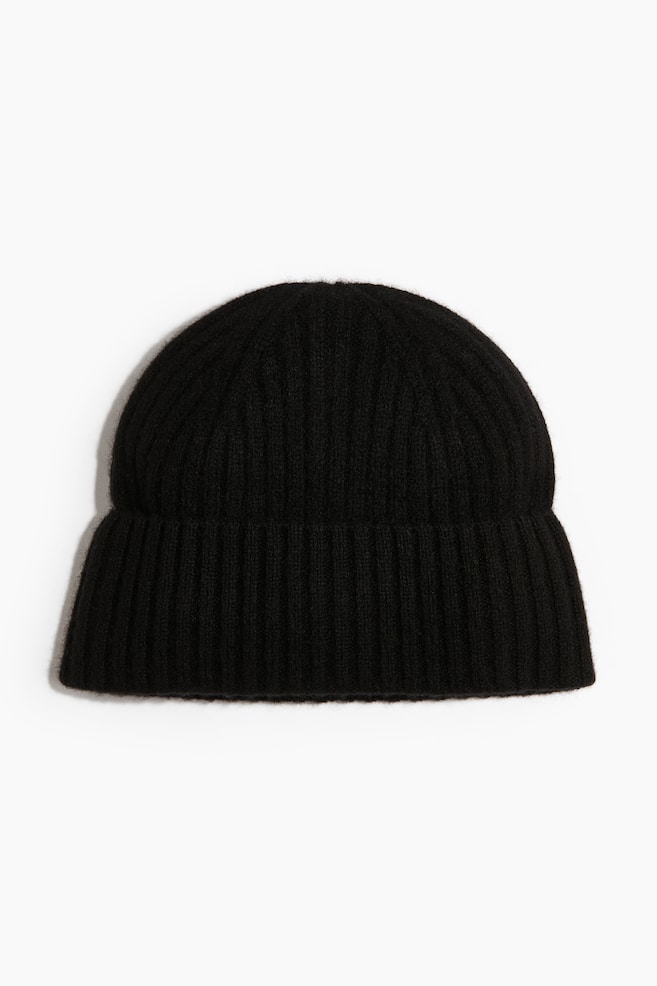 A black ribbed knit beanie is shown facing forwards, featuring a rounded crown and a wide, folded cuff. The hat displays a soft, slightly fuzzy texture with vertical ribbed detailing throughout. - 1