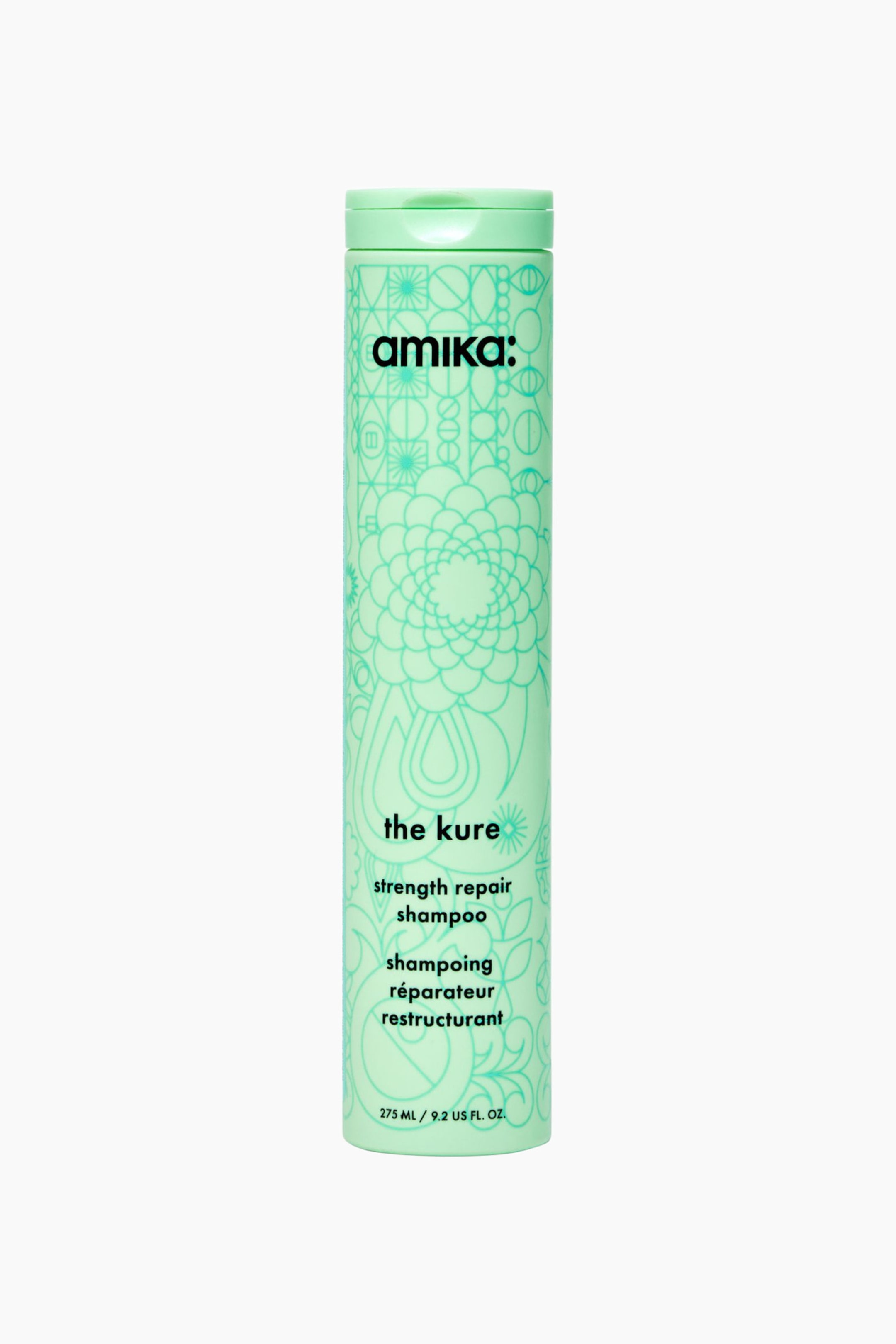 Visa större bild: En framifrånvy visar en hög, cylindrisk flaska med "amika: the kure strength repair shampoo" i en ljus mintgrön färg med ett matchande flip-top-lock. Flaskan har intrikata, mörkare gröna linjeillustrationer med blommiga och geometriska mönster samt svart text som visar varumärkesnamnet och produktinformationen.