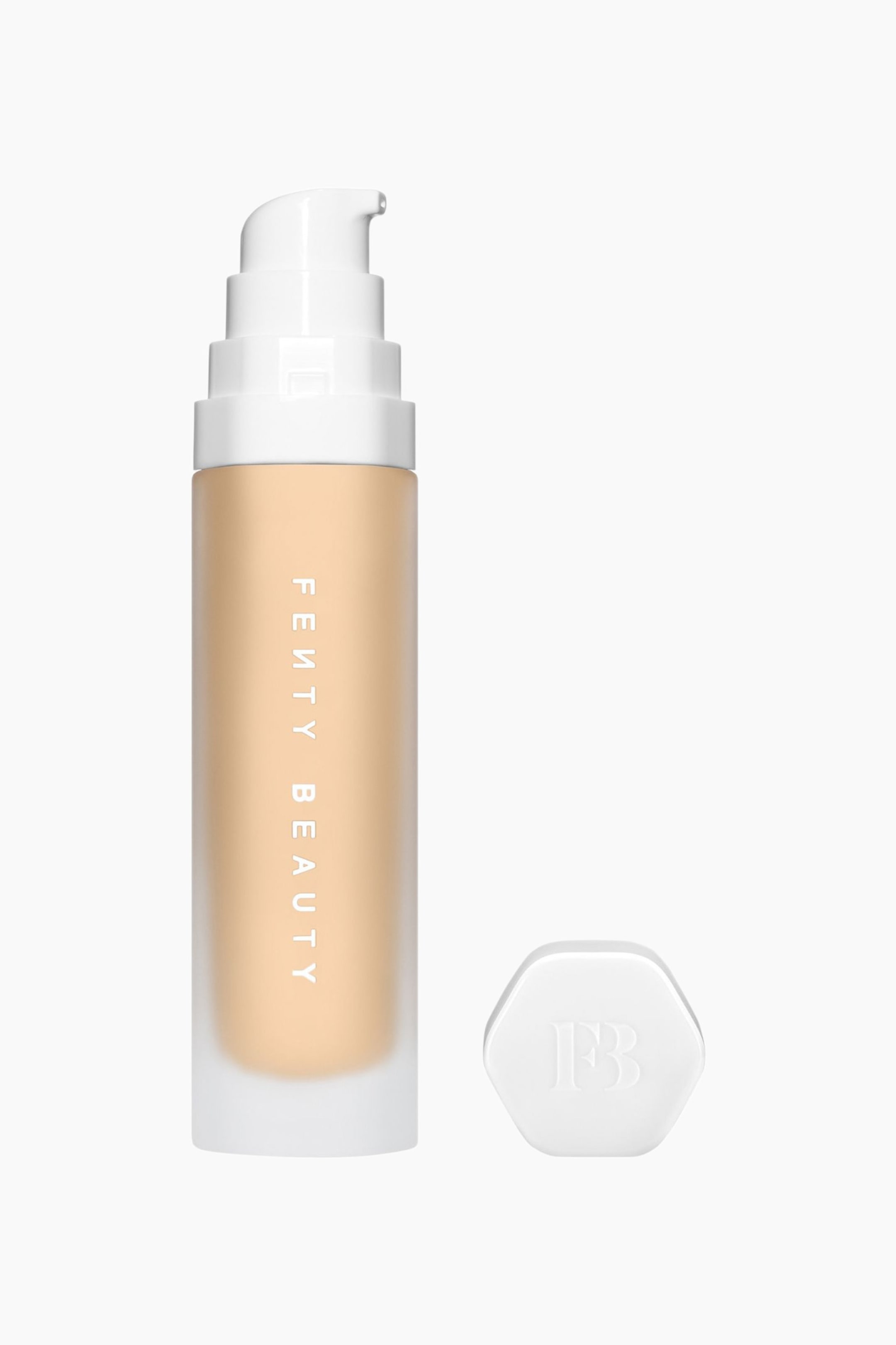 Visa större bild: Soft'lit Naturally Luminous Longwear Foundation står upprätt och visar en frostad cylindrisk flaska fylld med en ljusbeige vätska och med den vertikala texten ”FENTY BEAUTY”. En vit pumptopp sitter ovanpå flaskan, medan en separat vit sexkantig kork med en präglad ”FB”-logotyp ligger till höger.
