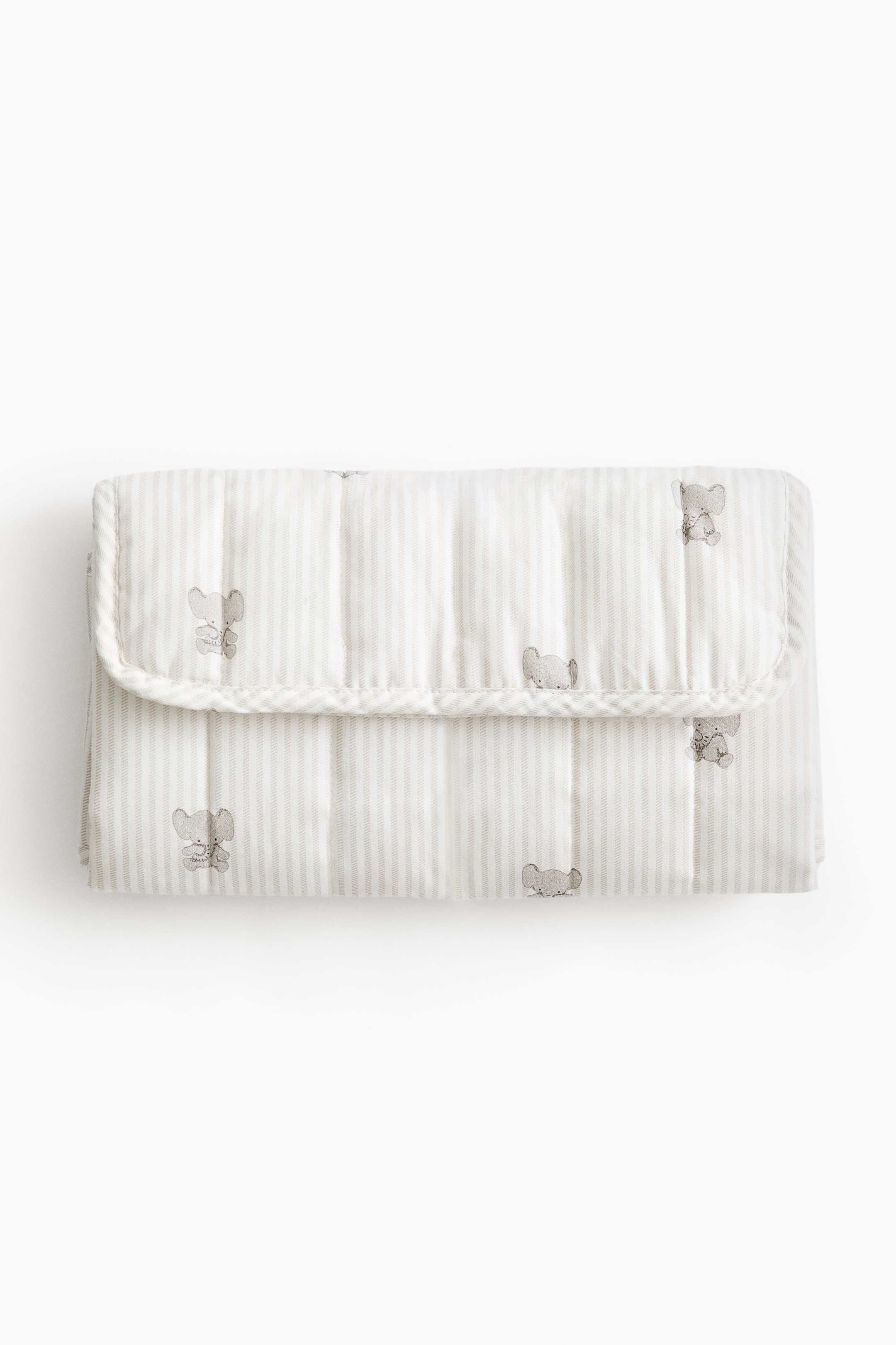View larger image: A folded, padded changing mat is shown from the front, featuring a light-colored quilted cotton weave with vertical stripes and a scattered print of small elephants. The rectangular mat is secured shut with a top flap that folds over the front.