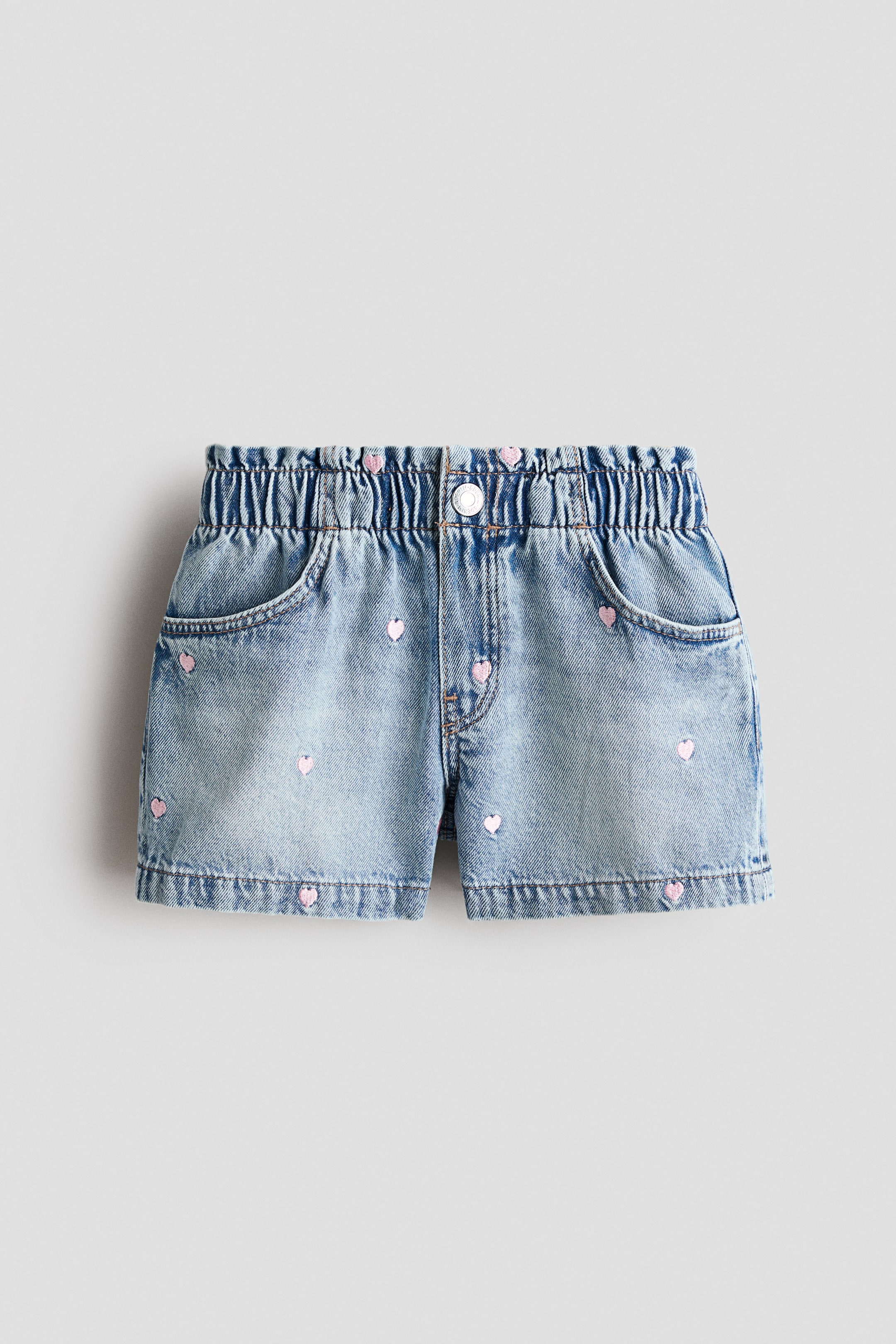 View larger image: Denim shorts are showcasing FRONT, featuring a light blue wash adorned with scattered pink embroidered hearts. Designed with an elasticated waistband, a single silver button closure, and two front curved pockets.