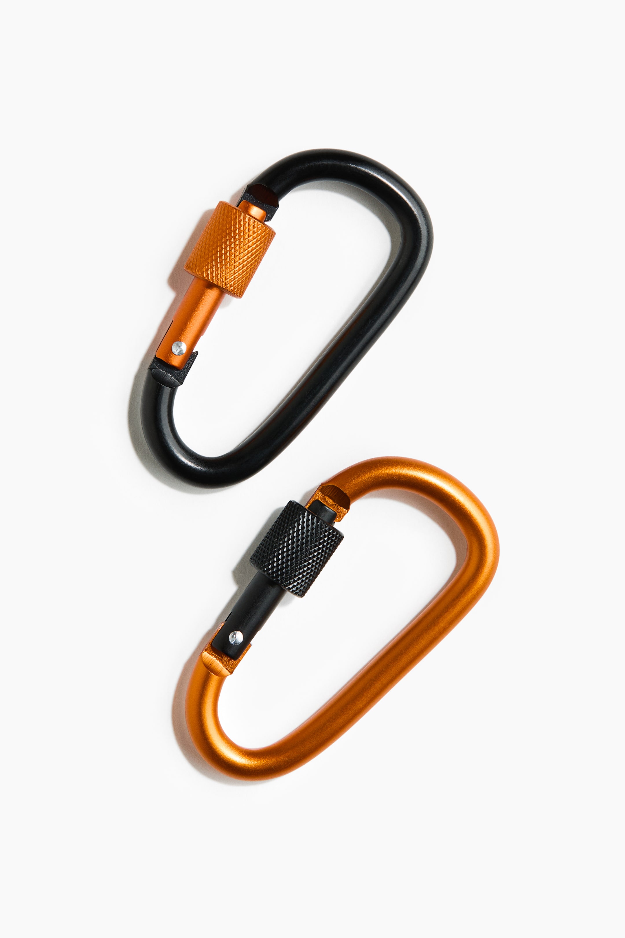 View larger image: Two D-shaped carabiners are positioned diagonally. The top carabiner is black with an orange knurled screw gate, while the bottom carabiner is orange with a black knurled screw gate.