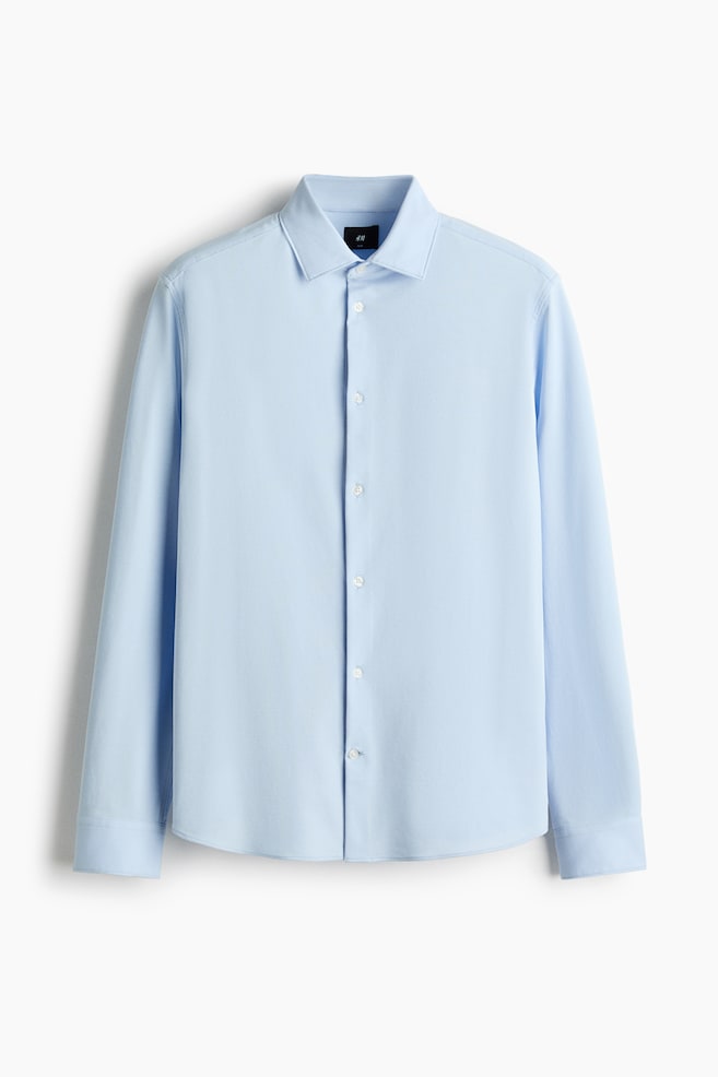 Une chemise bleu pâle affiche son DEVANT, avec un col pointu, une patte de boutonnage complète avec des boutons blancs, des manches longues avec des poignets à un bouton, et un ourlet arrondi. - 1