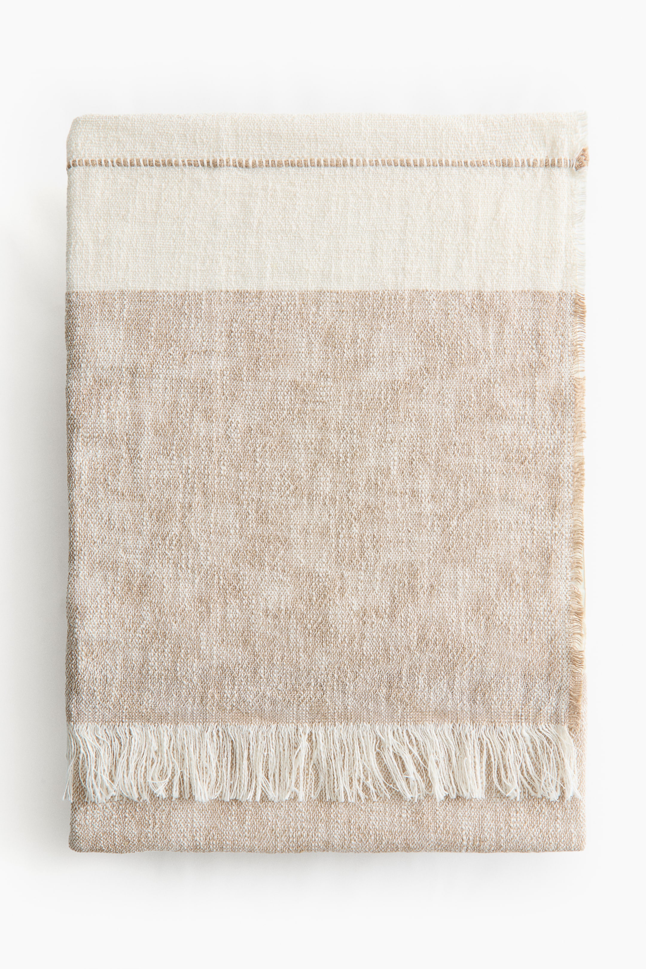 View larger image: A folded blanket displays a striped pattern in off-white and natural beige, made from a soft linen-and-cotton blend weave. It features frayed edges and fringes along its short sides.