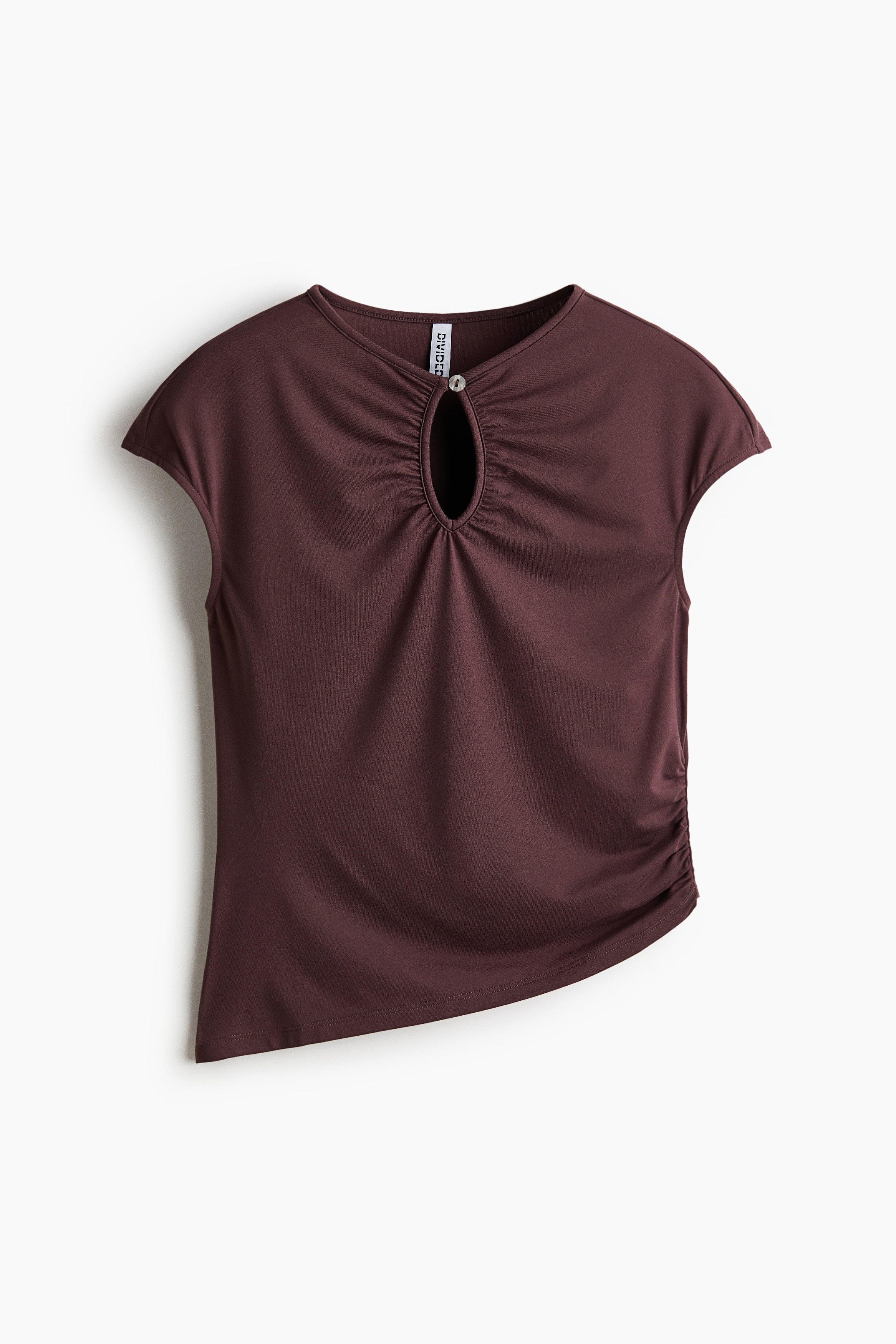 The model is wearing a fitted brown jersey top featuring a keyhole opening with gathered detailing at the neckline, cap sleeves, and a gathered side seam. The top has an asymmetrical hem and is styled with light beige denim jeans.