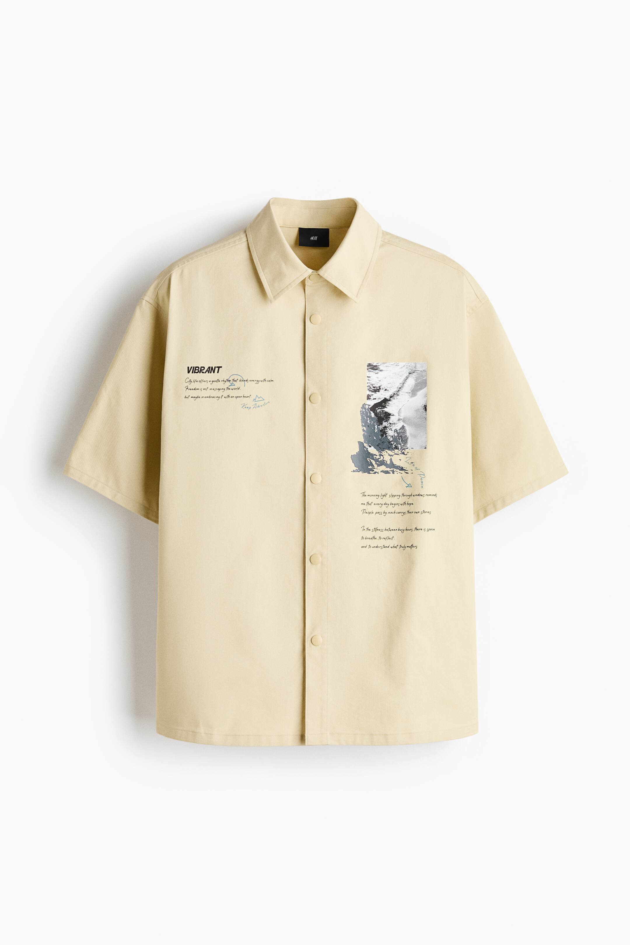 View larger image: A light yellow, short-sleeve shirt is facing front, showcasing a classic point collar, a snap-button front closure, and a straight hem. The shirt features black graphic text on the right chest and a rectangular grayscale landscape print with cursive text on the left side.