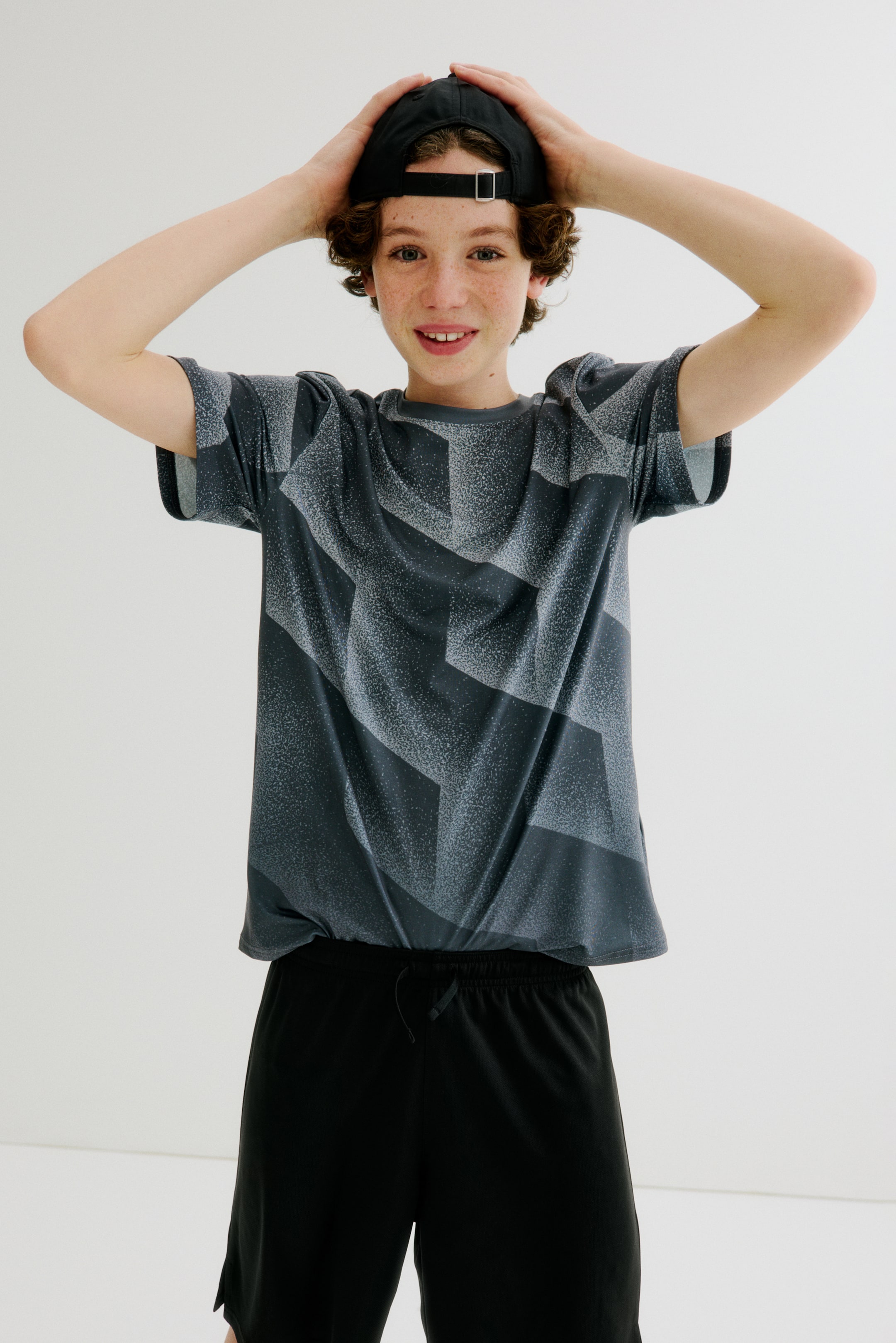 View larger image: A dark grey, short-sleeved t-shirt is presenting a geometric pattern in lighter grey with a speckled texture, and it is styled with black athletic shorts featuring a drawstring waist. Both garments are appearing loose-fitting and are facing front.
