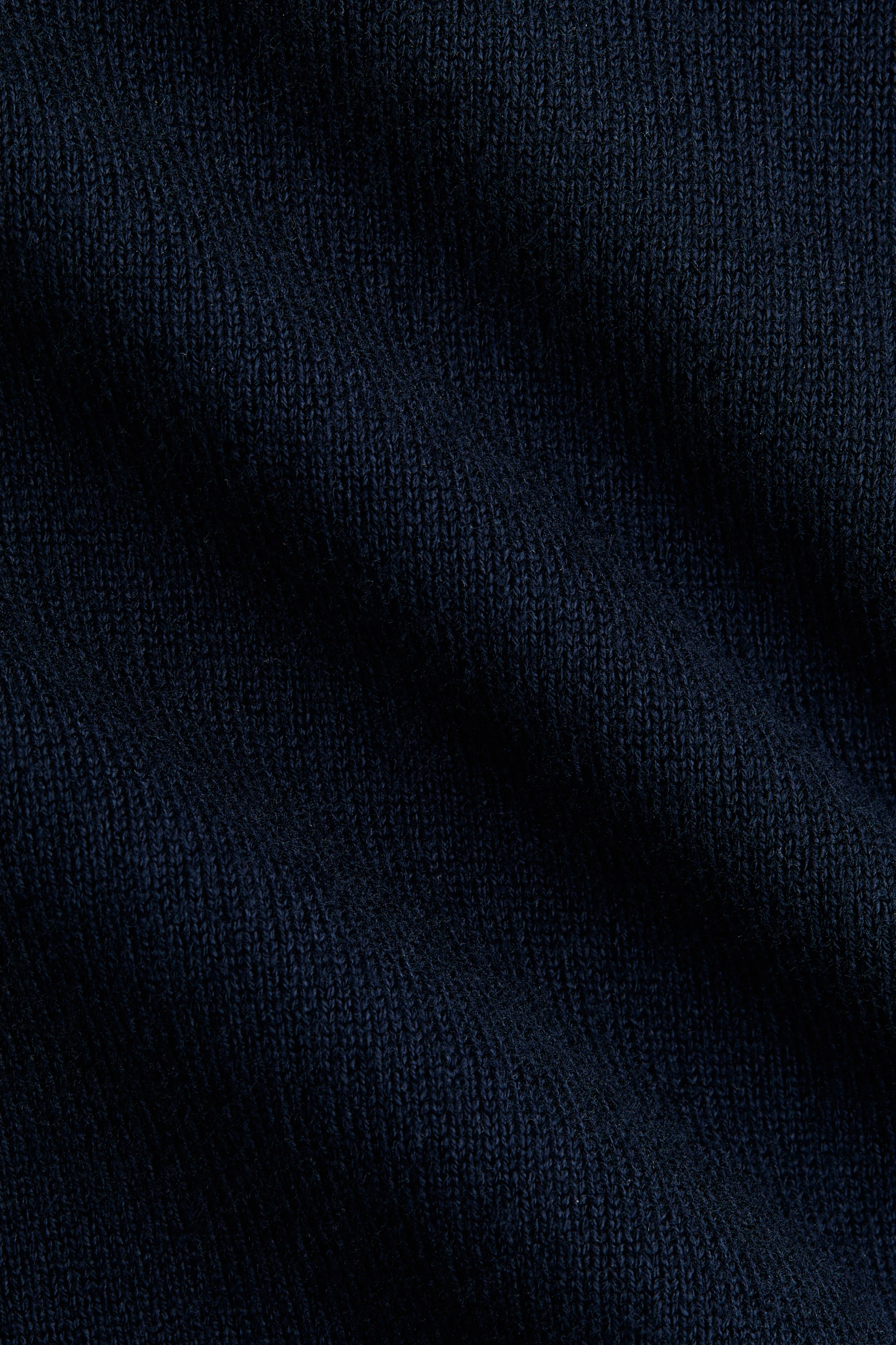 Größeres Bild ansehen: Ein dunkelblauer, fein gestrickter Stoff zeigt eine gerippte Struktur. Das Material bildet sanfte Falten und Schatten.