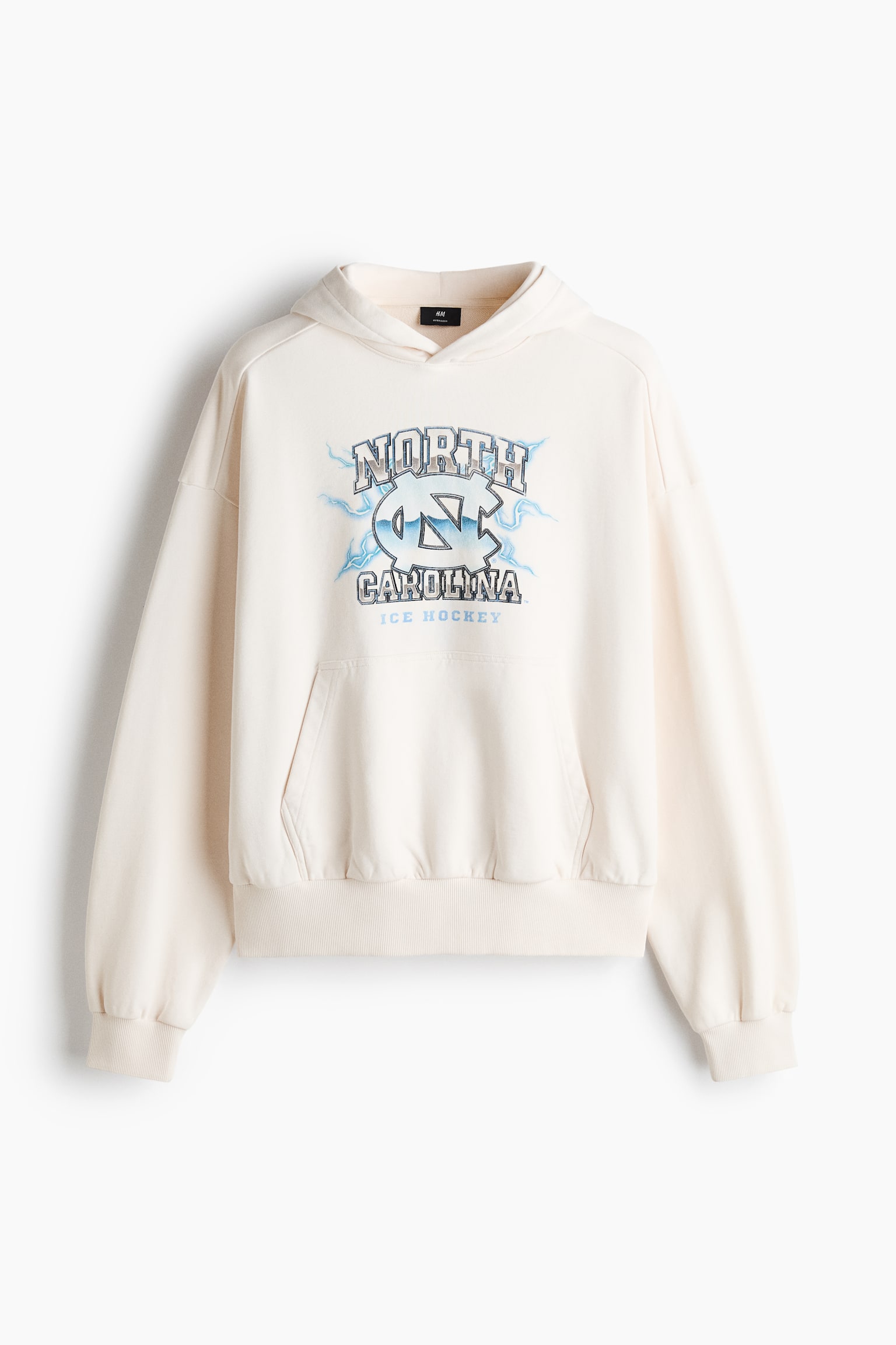 A cream-coloured hoodie is shown from the front, featuring dropped shoulders, ribbed cuffs, a ribbed hem, and a front kangaroo pocket. The chest displays a graphic print of an interlocking "NC" logo surrounded by "NORTH CAROLINA ICE HOCKEY" text and light blue lightning bolt details.