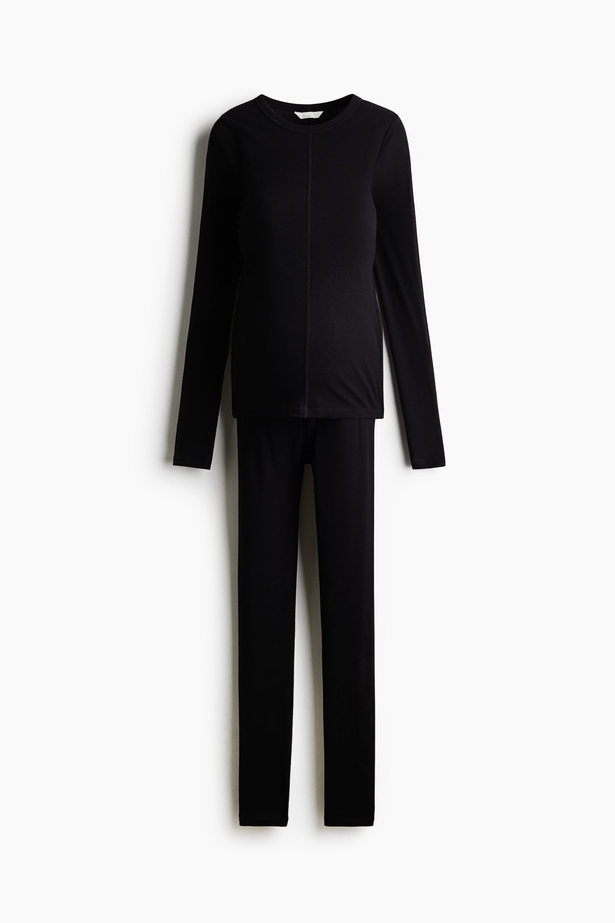 Größeres Bild ansehen: Ein schwarzes Set aus geripptem Jersey mit Oberteil und Leggings ist von vorne zu sehen. Das figurbetonte Oberteil verfügt über einen Rundhalsausschnitt, lange Ärmel und eine markante vertikale Flatlock-Naht in der Mitte, während die dazu passenden schmal geschnittenen Leggings gerade nach unten verlaufen.