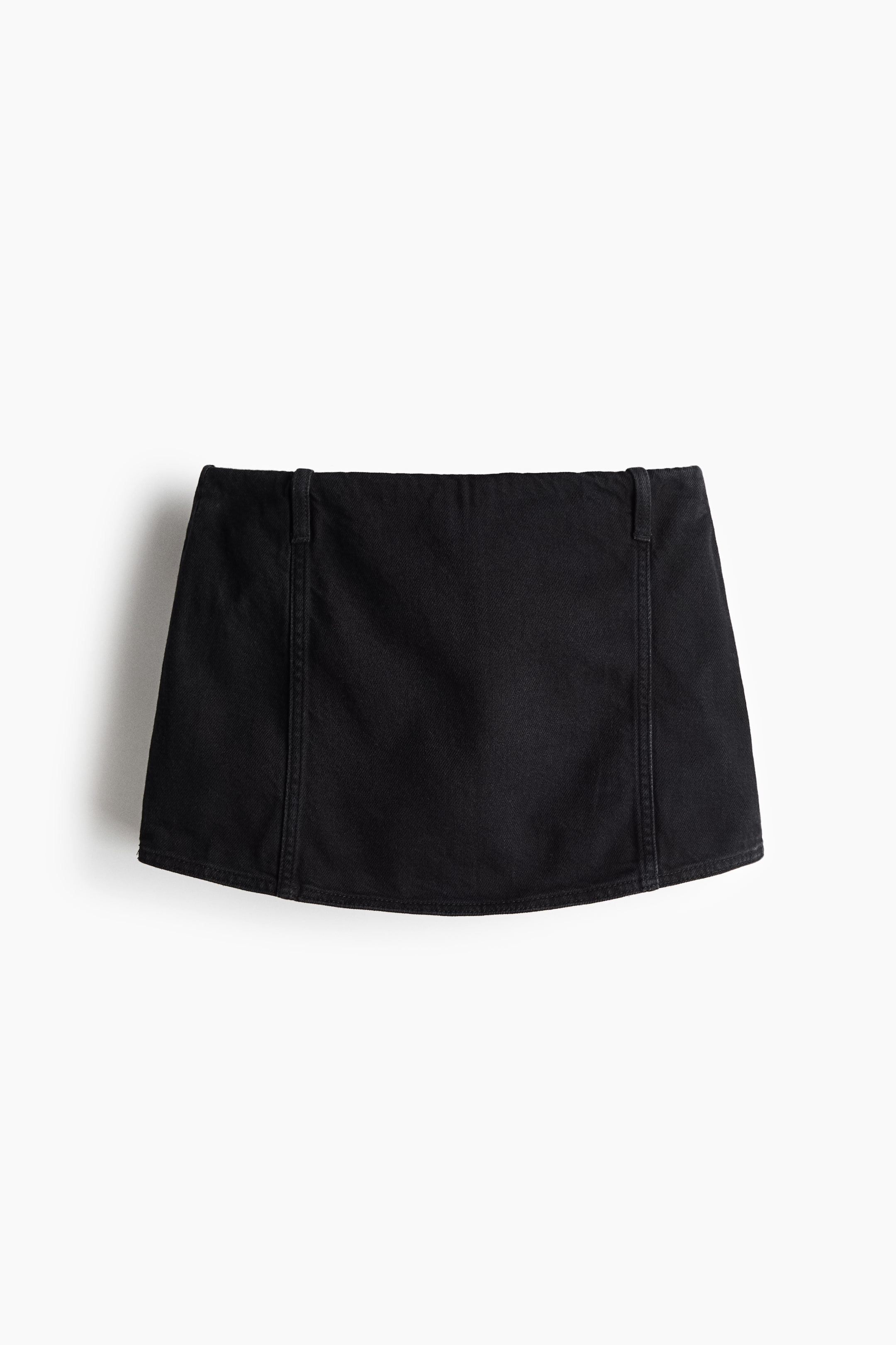 View larger image: A black denim mini skirt is shown from the front, featuring a flat waistband, two small belt loops at the top, and vertical seams on the front panel. The bottom hem is subtly curved.