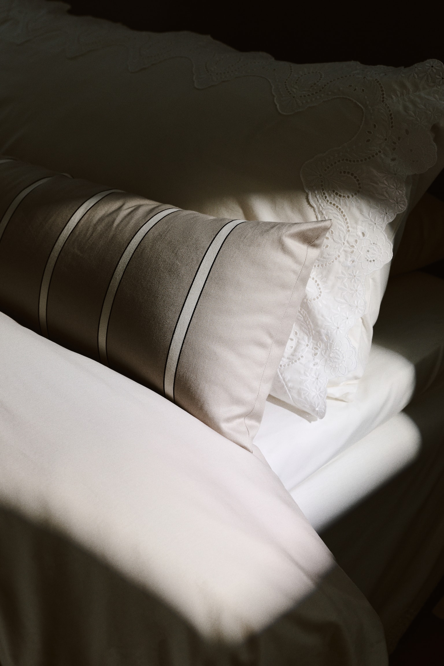 A long, light beige body pillow features a pattern of vertical stripes, each stripe showcasing a central white band bordered by thin black lines on either side. - 1