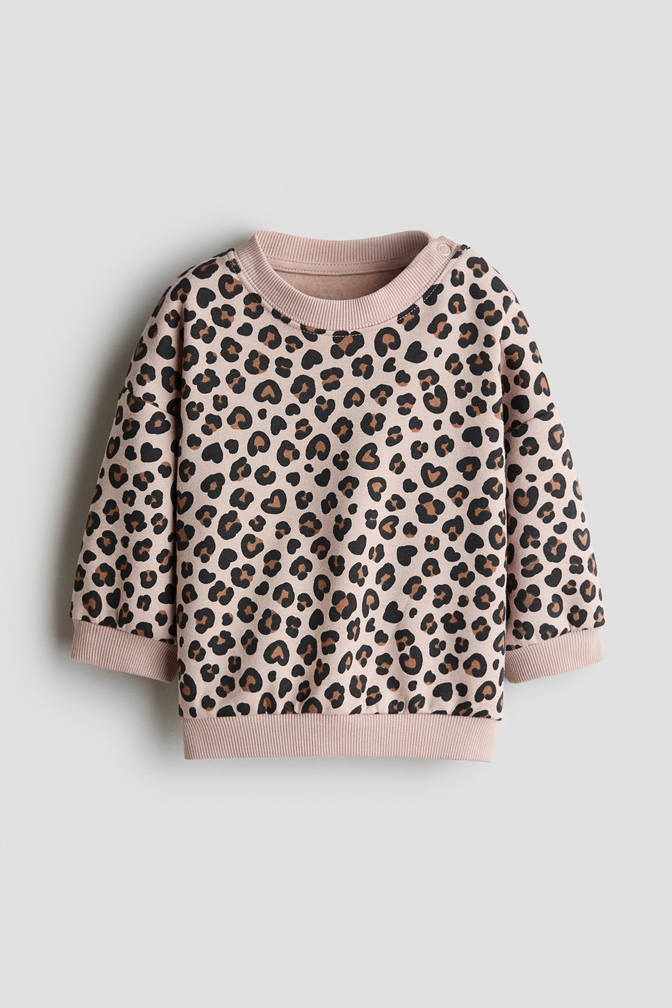 View larger image: A printed sweatshirt showcasing a black and brown leopard print on a light pinkish-beige fabric, displayed from the front with a crew neck, ribbed cuffs, a ribbed hem, and two snap buttons on the left shoulder.