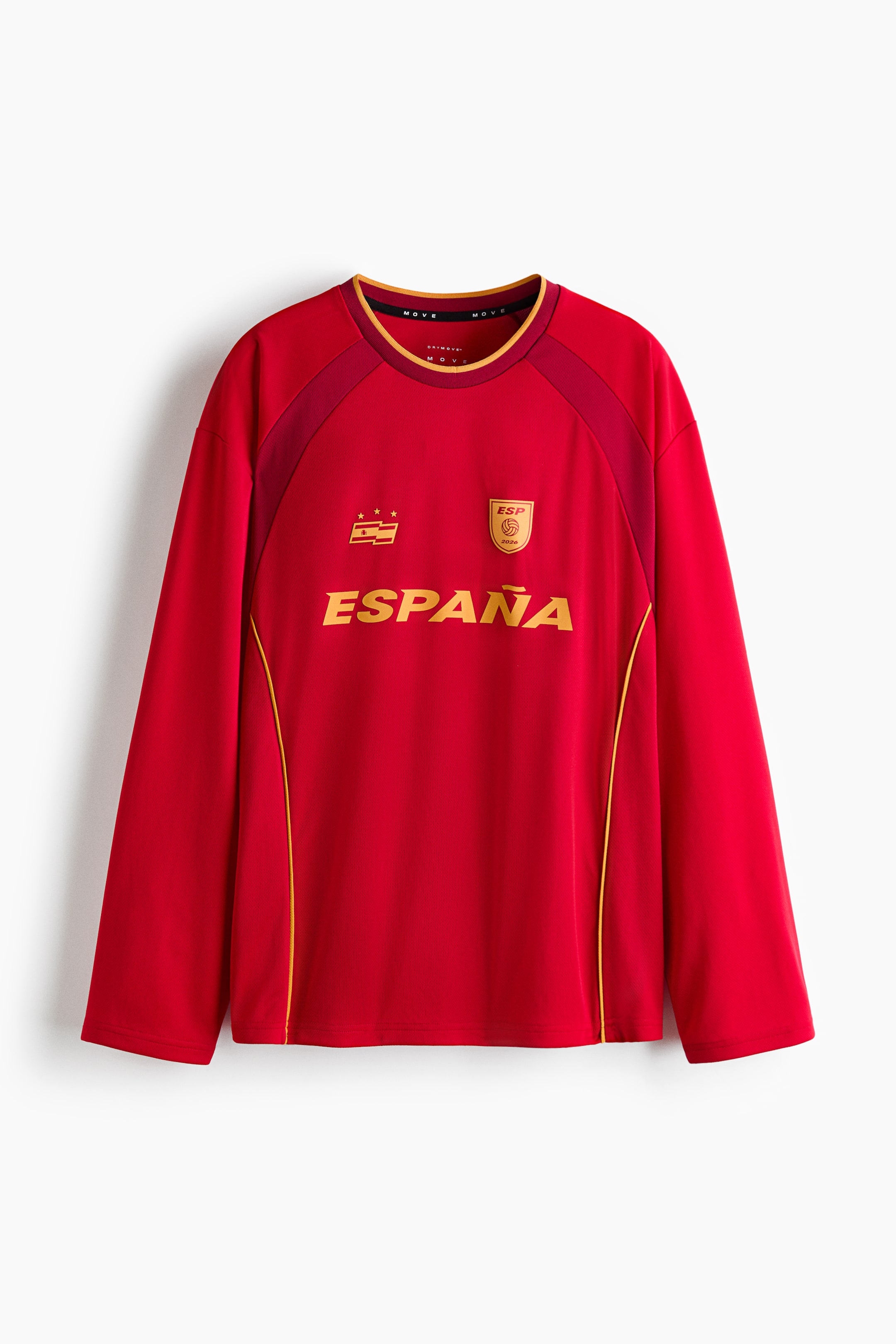 Voir une image plus grande: Une chemise rouge à manches longues est présentée de face, avec un col rond orné de bordures jaunes et rouge foncé. Le devant affiche "ESPAÑA" en lettres dorées, un emblème rectangulaire avec des étoiles, un emblème en forme de bouclier, des panneaux d'épaule rouge foncé, et de fines rayures dorées courant verticalement le long des côtés.