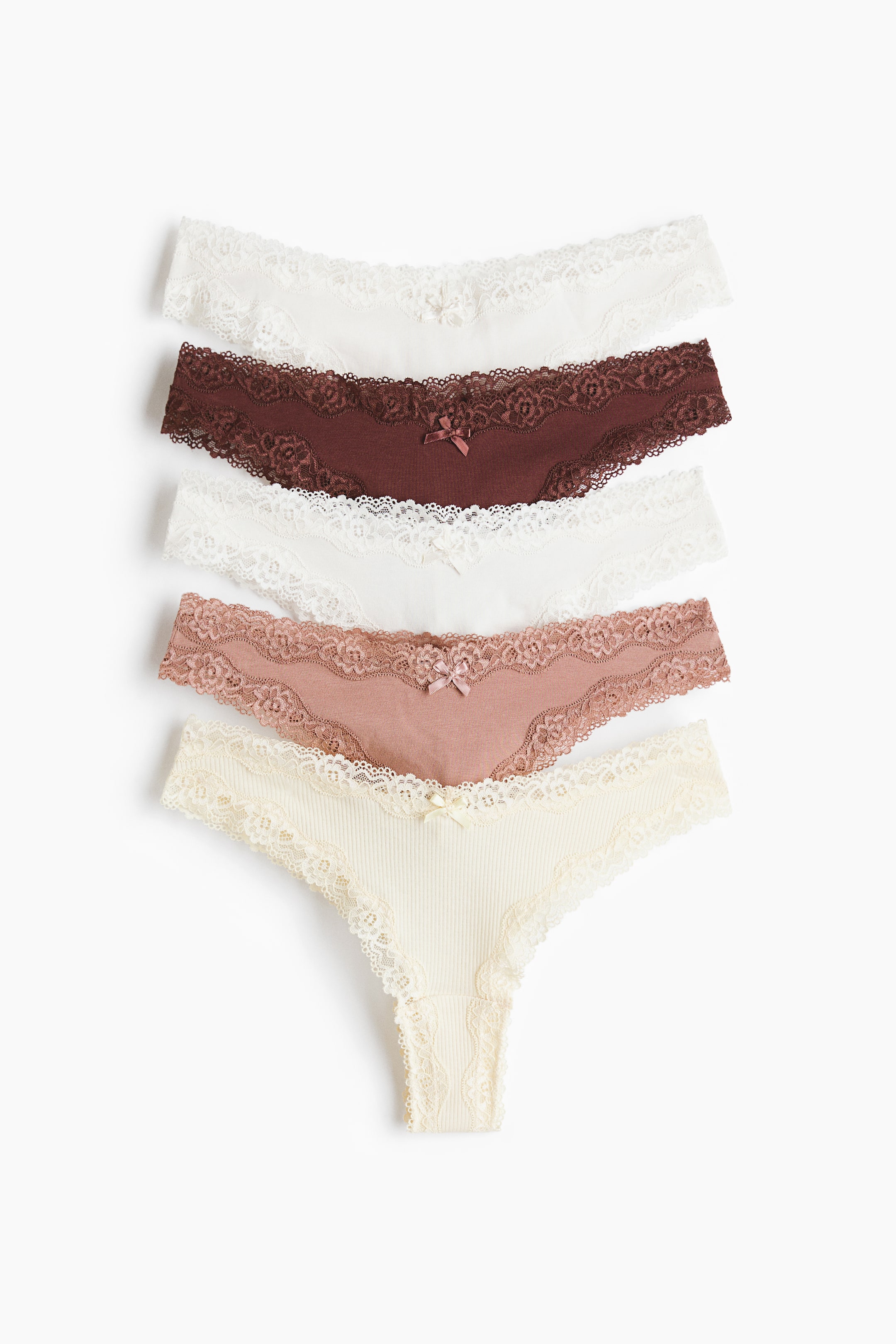 拡大画像を表示: コットンジャージーとレースで作られた5枚のブリーフが、わずかに重なり合った状態で前面に並んでいます。各ブリーフは、ミッドのV字型ウエストにレーストリムが施され、中央前部には小さなリボンが付いています。セットには、ホワイト、ダークブラウン、ダスティローズ、リブクリームカラーのブリーフが含まれています。
