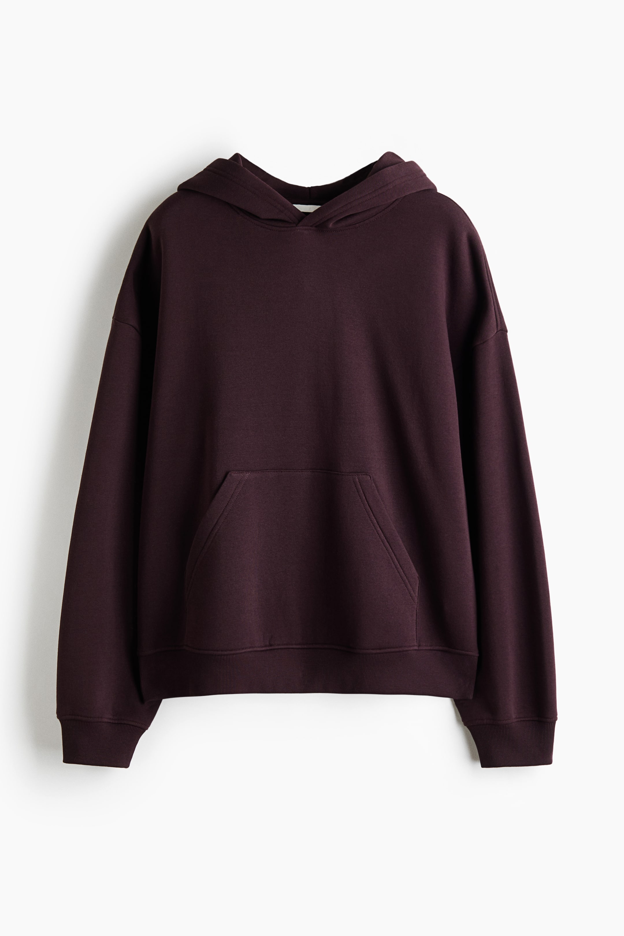 Grotere afbeelding bekijken: Een donker bordeauxkleurige hoodie hangt recht van voren en laat de losse pasvorm zien met lage, afhangende schouders en een dubbelgelaagde capuchon. Het ontwerp heeft een kangoeroezak aan de voorkant en is afgewerkt met geribde boorden en een geribde zoom.