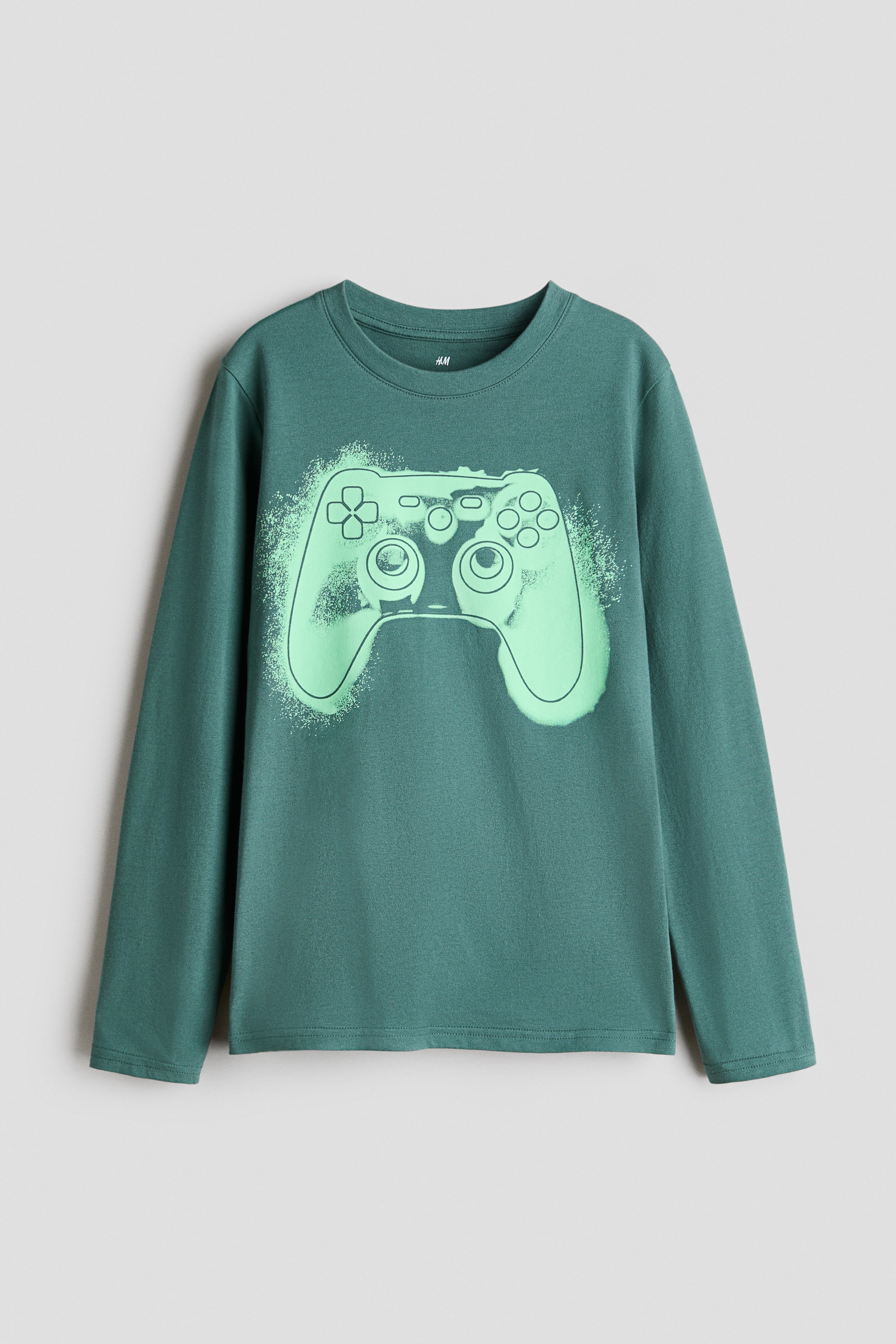 Größeres Bild anzeigen: Ein langärmeliges T-Shirt in Türkisgrün liegt flach und zeigt die Vorderseite. Es verfügt über ein großes, hellgrünes Grafikmotiv eines Gaming-Controllers auf der Brust und hat einen gerippten Rundhalsausschnitt mit schlichten Bündchen und einem schlichten Saum.