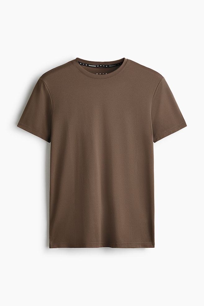 A brown muscle fit sports top is displaying its front, featuring a subtle, all-over textured pattern. It is presenting a crew neck, short sleeves, and a straight hem with small side slits, while 'TRAINING MOVE' text is visible on the inside of the collar band. - 1