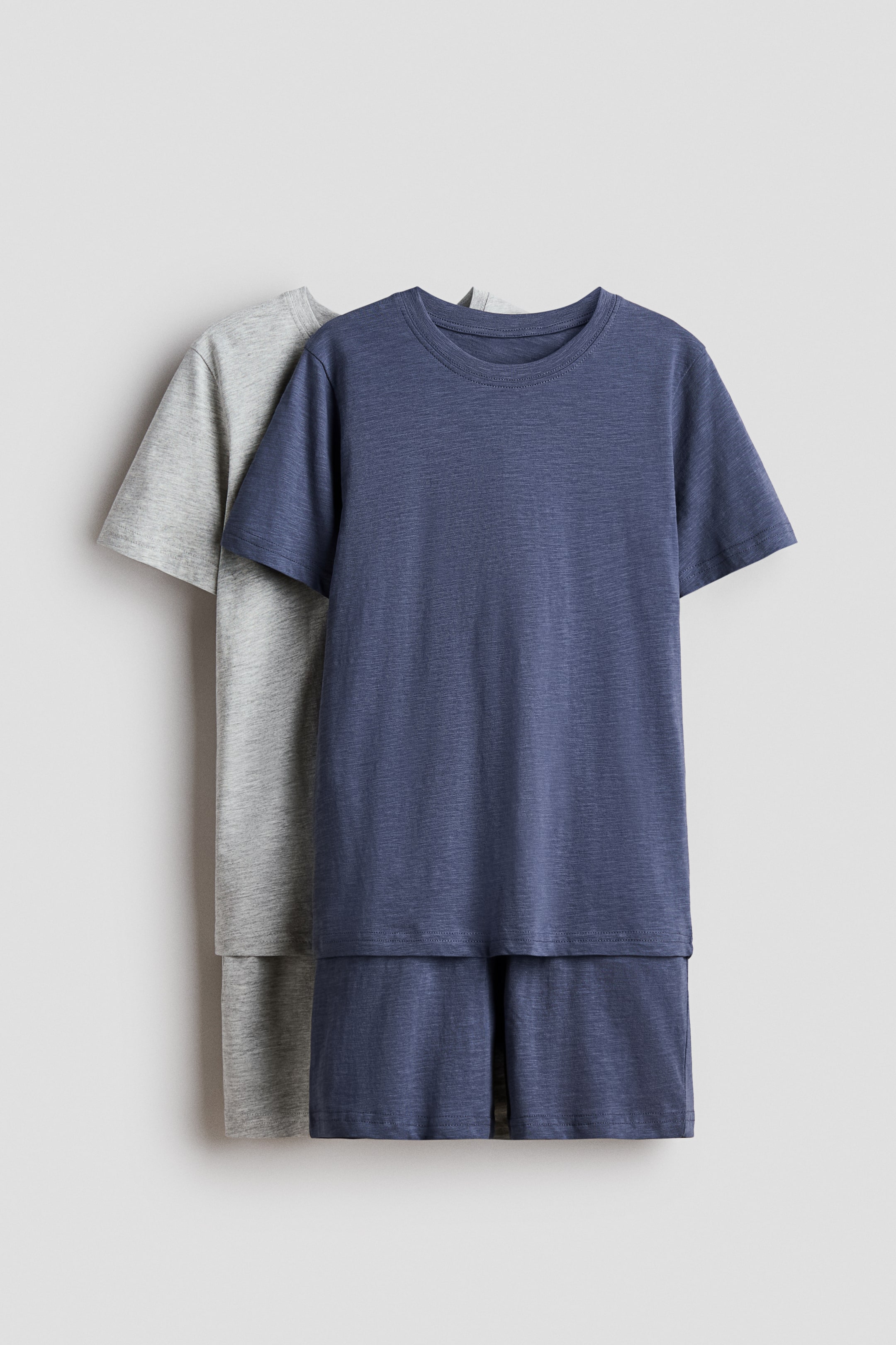View larger image: Two short-sleeved T-shirt and shorts sets are displayed front-facing, with a dark blue set positioned in front of a light grey set. Both T-shirts are designed with crew necks, and the fabric of both sets exhibits a subtle heathered texture.