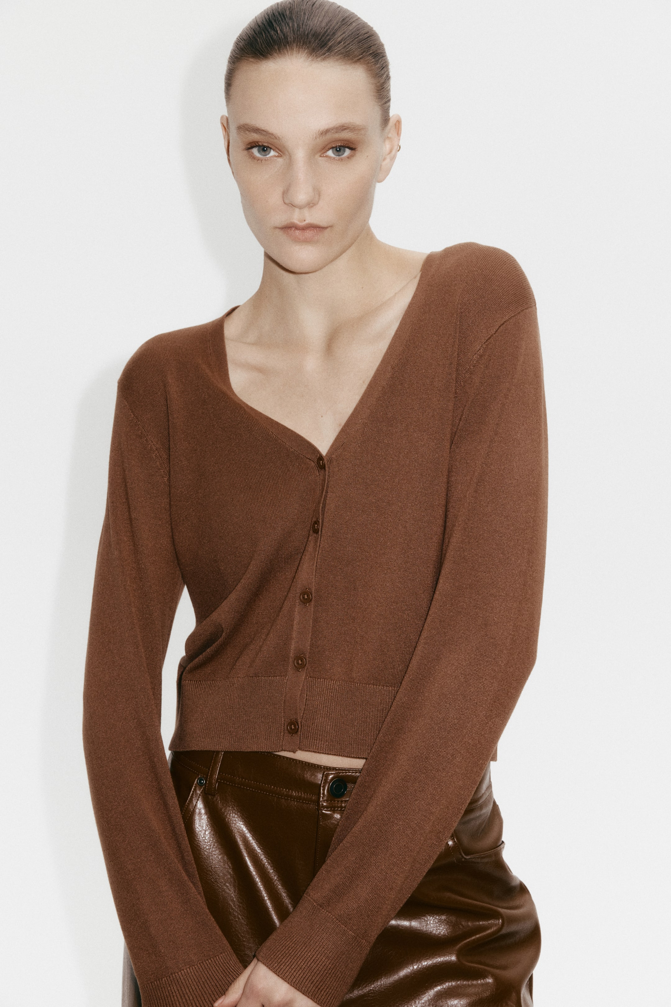View larger image: A brown knit cardigan featuring a wide V-neckline and a button-front closure with matching buttons. Designed with long sleeves, ribbed cuffs, and a ribbed hem, it comes in a chic cropped length.