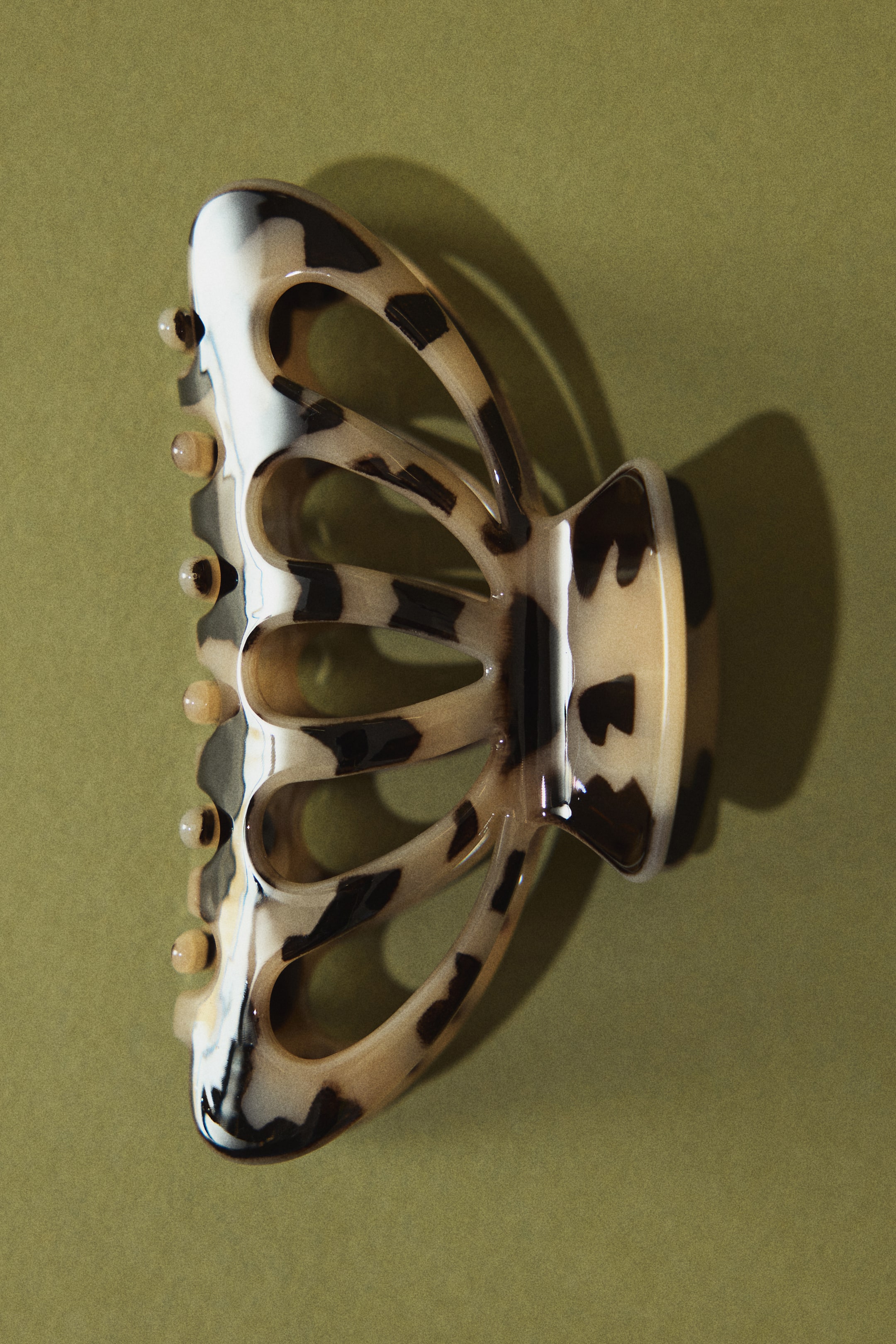 Visa större bild: En hårklo uppvisar ett krämvitt och mörkbrunt sköldpaddsmönster och har en böjd, genombruten design. Den ligger på sidan och visar sina inlåsande tänder och sin gångjärnsmekanism.