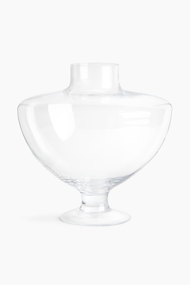 A large, footed vase, facing front, crafted from clear glass. It showcases a rounded, bulbous body that narrows at the top into a cylindrical opening, and is supported by a short, circular foot. - 1