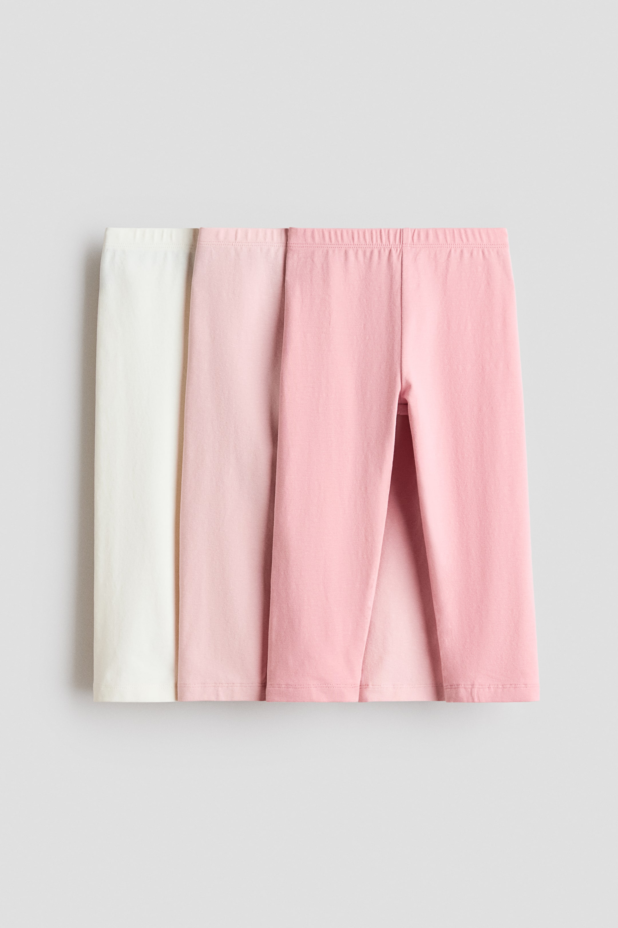 Agrandir l'image: Trois paires de leggings 3/4 en jersey de coton doux sont présentées de face. Elles disposent de tailles élastiquées et sont proposées en blanc, rose clair et rose moyen, se chevauchant partiellement.