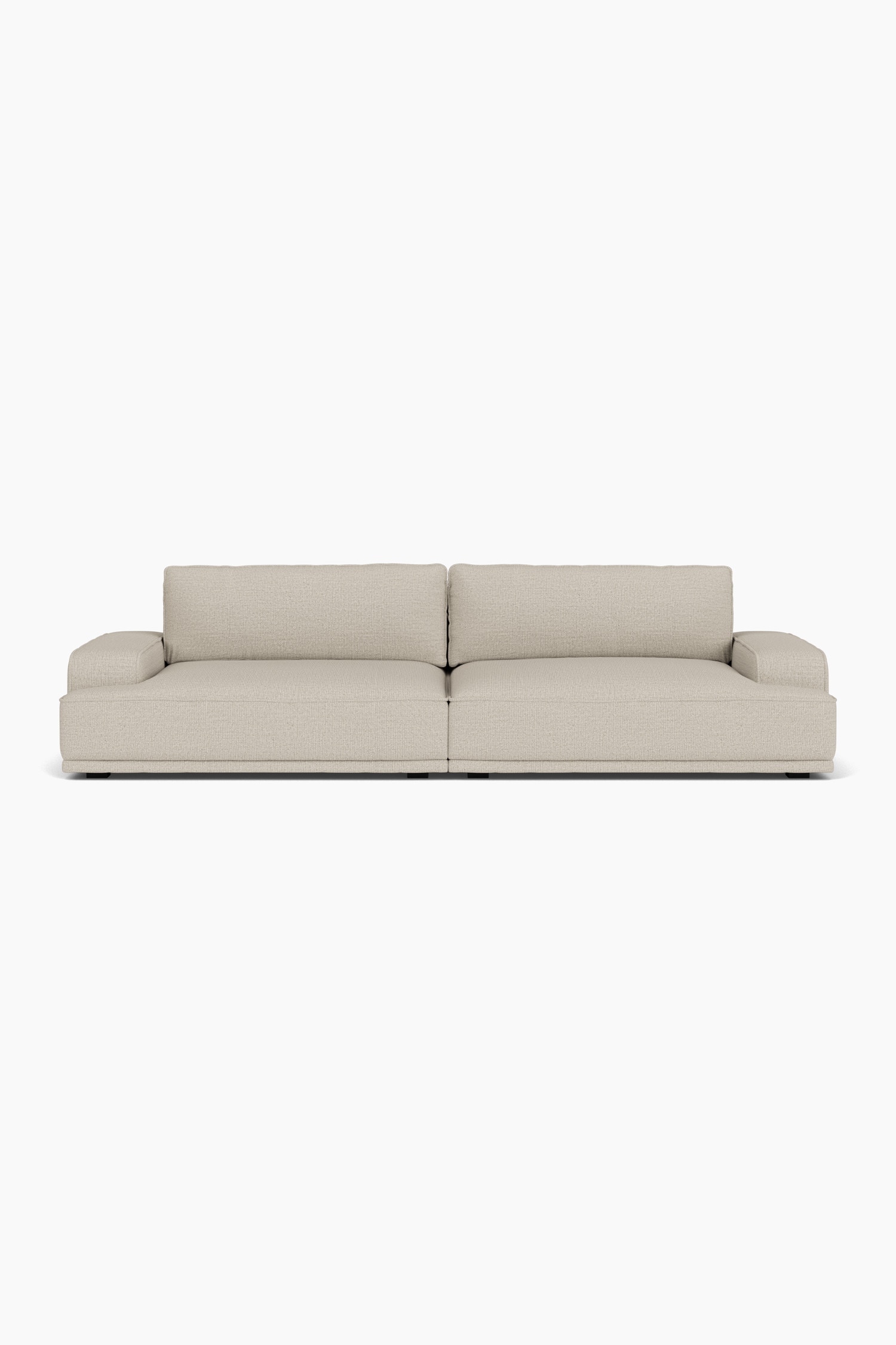 Un canapé modulaire bas, revêtu dâun tissu texturé beige clair, est orienté vers lâavant et présente des accoudoirs de style bloc, de profonds coussins et trois coussins décoratifs assortis. Un ottoman carré coordonné, dans le même tissu, est placé devant le côté gauche du canapé.