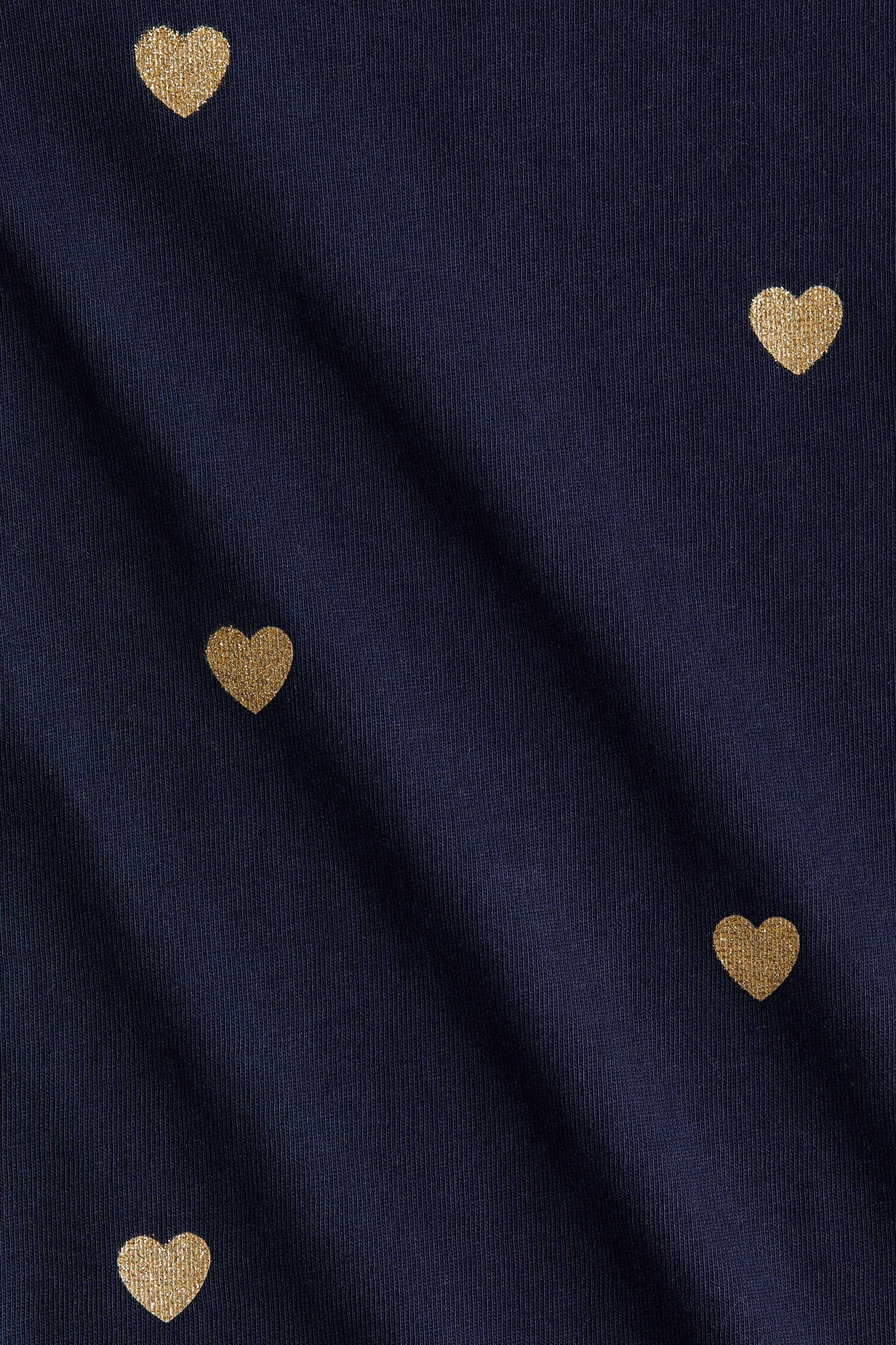 View larger image: A close-up of a top in soft cotton jersey is being shown, highlighting its navy blue fabric with scattered golden glitter heart shapes. The material is exhibiting a fine knit texture and subtle folds.
