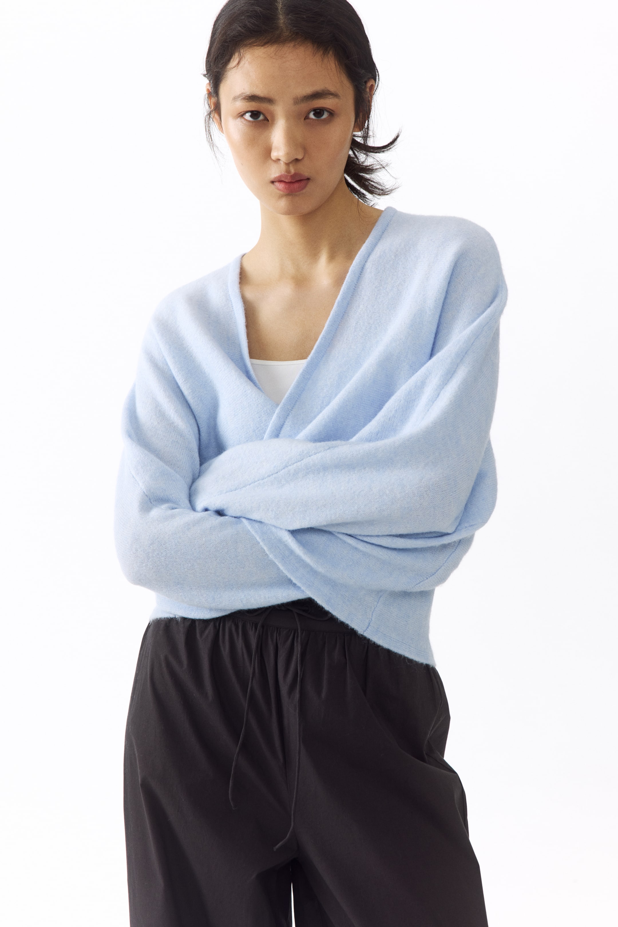View larger image: A light blue wrap cardigan showcases a soft, fuzzy texture and a deep V-neck, with its front panels elegantly wrapping across the body. It features long, loose sleeves with ribbed cuffs and a ribbed hem, and is layered over a white top.