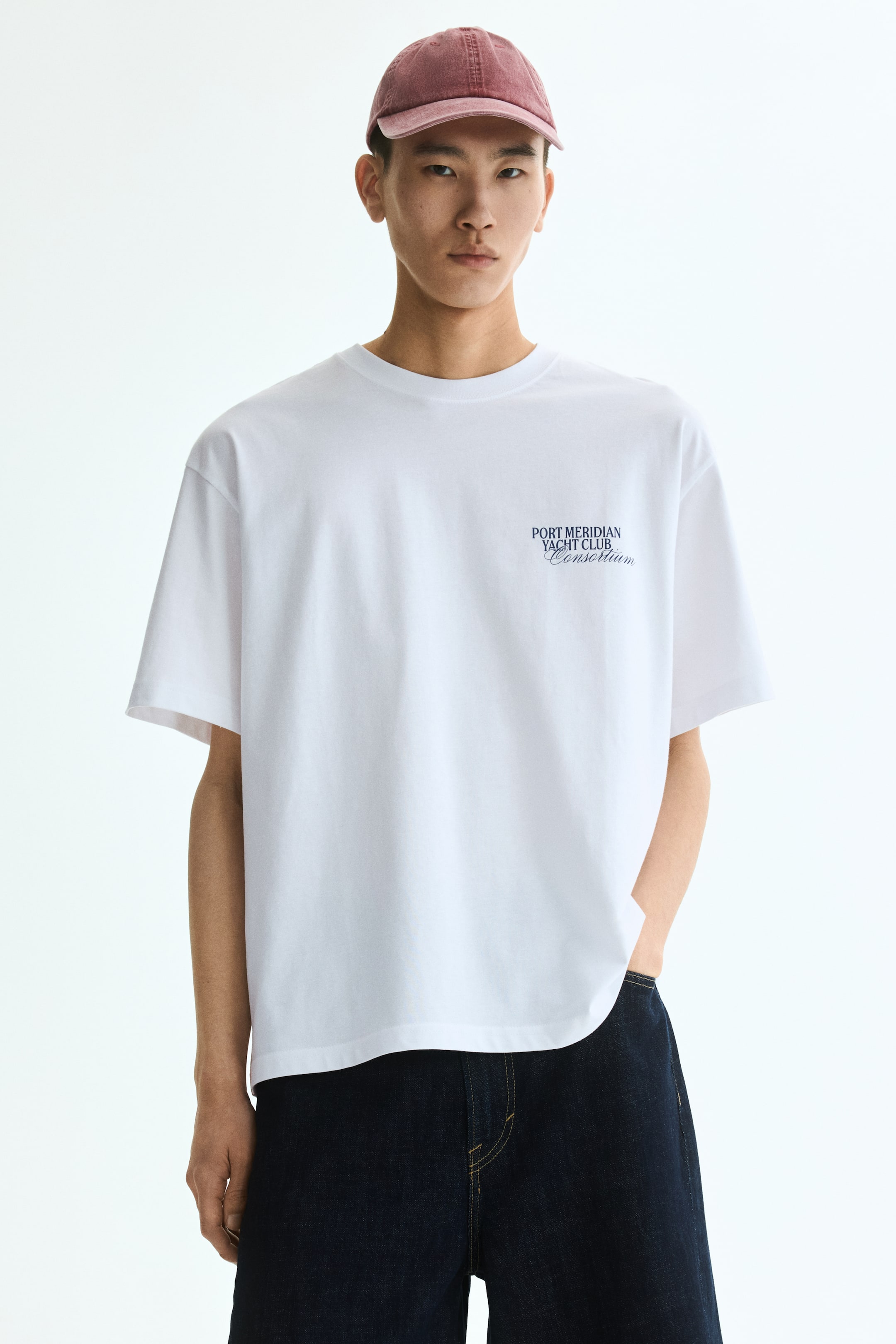 Größeres Bild ansehen: Ein weißes Baumwolljersey-T-Shirt zeigt seine Vorderseite mit einem runden, gerippten Ausschnitt und überschnittenen Schultern. Es präsentiert einen lockeren Schnitt, und dunkelblaue Schrift mit dem Text "PORT MERIDIAN YACHT CLUB Consortium" erscheint auf der linken Brust.