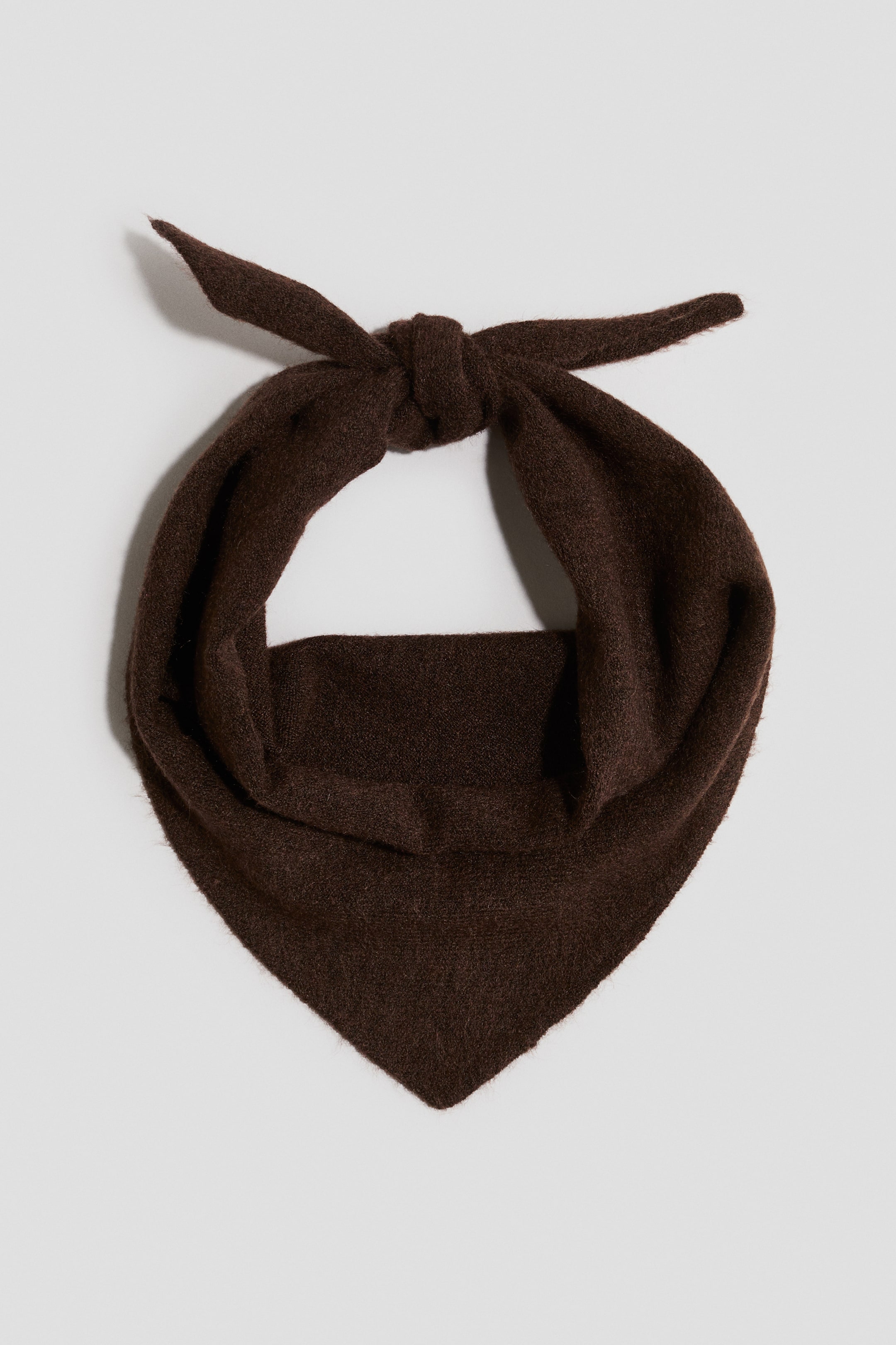 View larger image: A dark brown triangular scarf features a knot at the top, with two short ends extending outwards, showcasing its soft, textured knit.