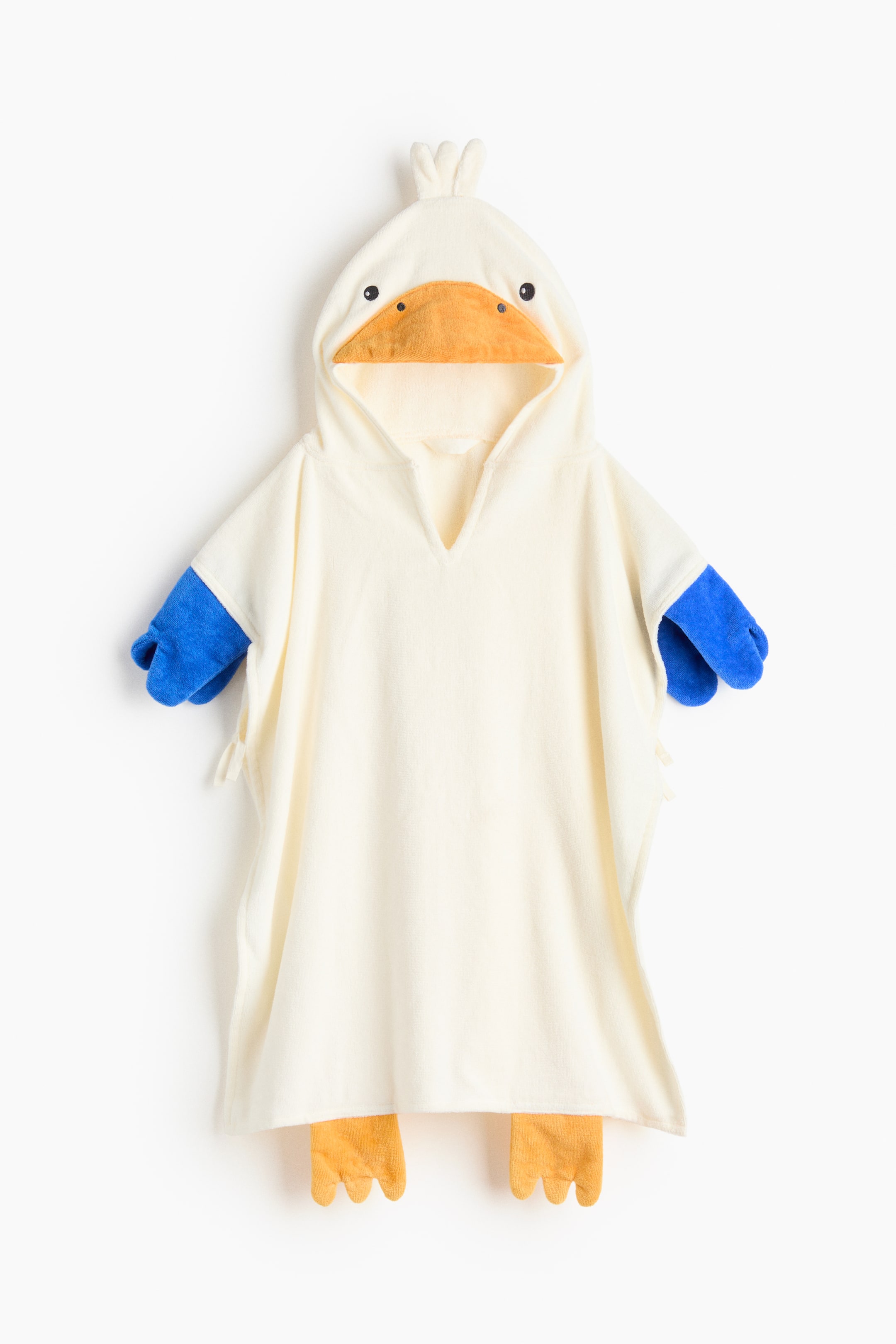 拡大画像を表示: タオルケープ、FRONT は、オフホワイトのポンチョスタイルの衣服で、オレンジ色のくちばし、黒い目、白い房毛が特徴のアヒルの頭をデザインしたフードが付いています。両側からは青いミトンのような形が現れ、裾からはオレンジ色の水かきの足が突き出ています。